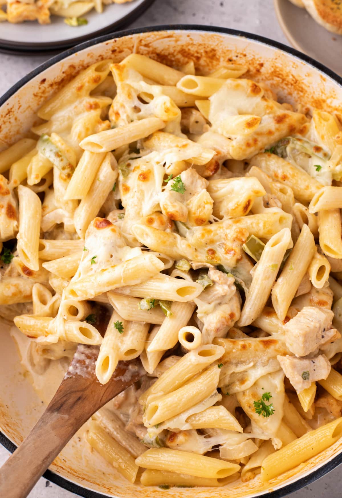 Chicken Philly cheesesteak pasta served as an easy weeknight dinner with garlic bread Overhead view of skillet of chicken Philly cheesesteak pasta with serving spoon and plates of pasta and bread