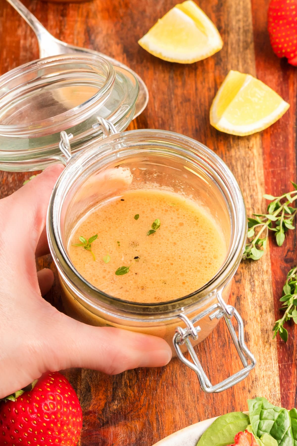 Jar of honey Dijon dressing on a wooden board with lemon wedges and thyme