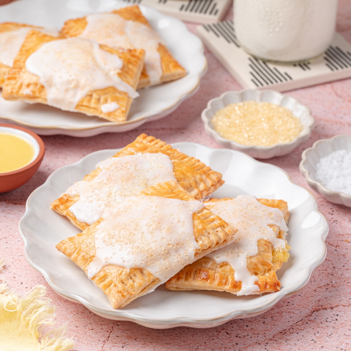 Plates of lemon toaster pastries served with milk and glaze, surrounded by ingredients 