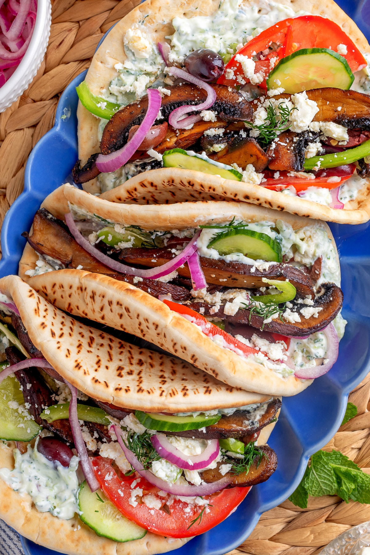 Overhead of finished mushroom gyros with full toppings Overhead shot of finished gyros topped with vegetables and tzatziki on a blue platter.