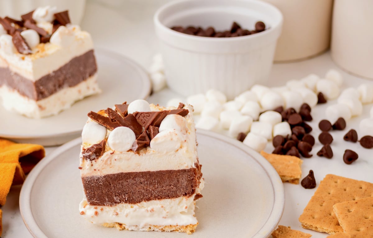 Frozen s’mores lasagna slice on a plate with graham crackers and marshmallows scattered nearby