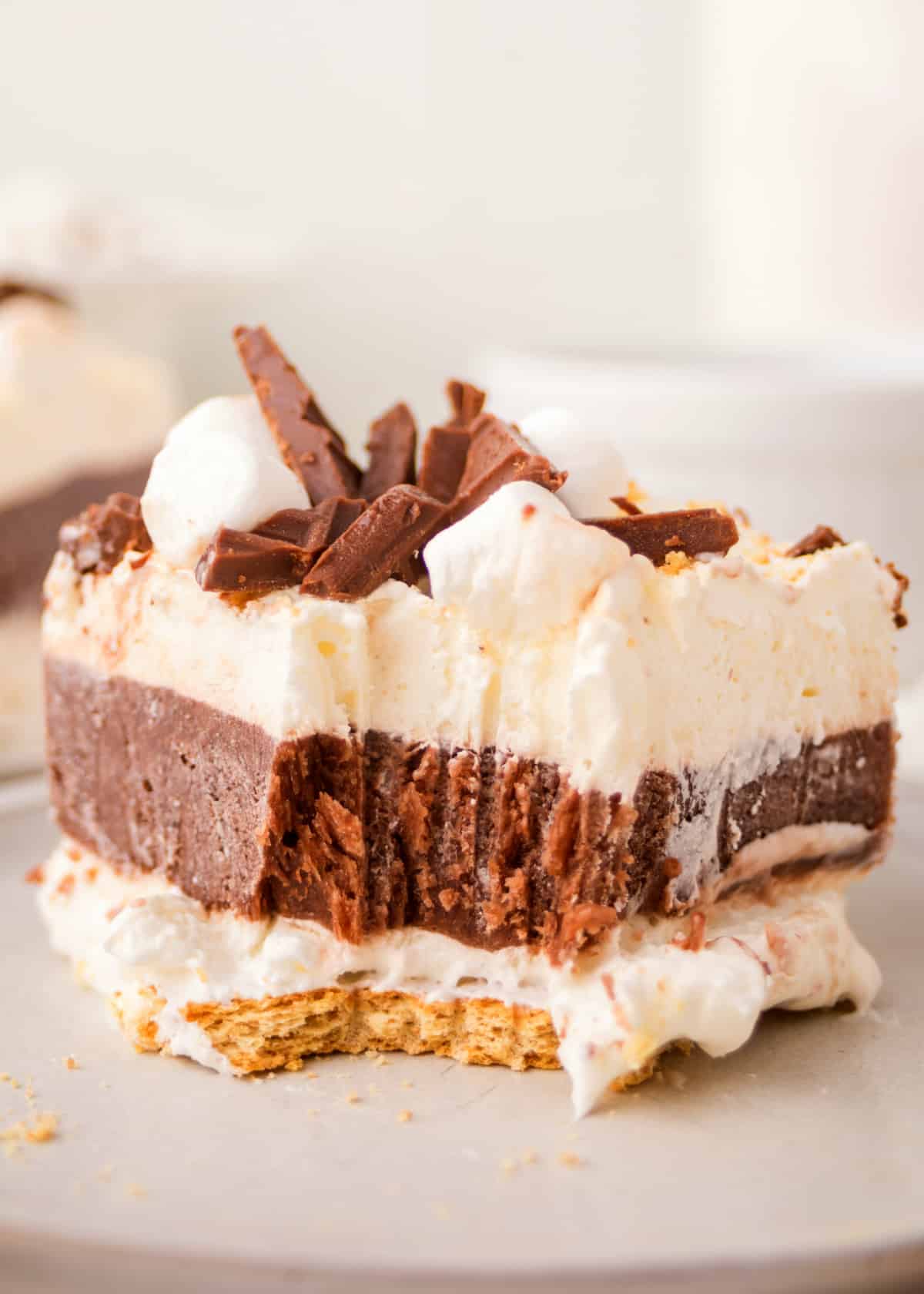 Close-up of a sliced frozen s’mores lasagna with chocolate, marshmallow, and graham cracker layers with a bite out