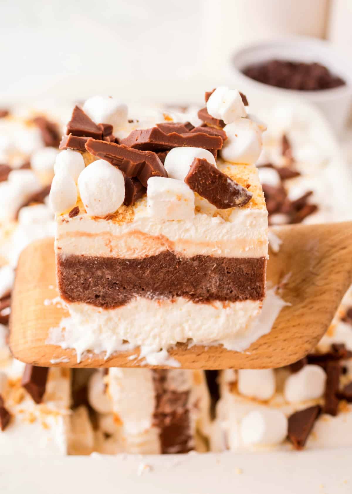 Wooden spatula lifting a slice of frozen s’mores lasagna from the pan