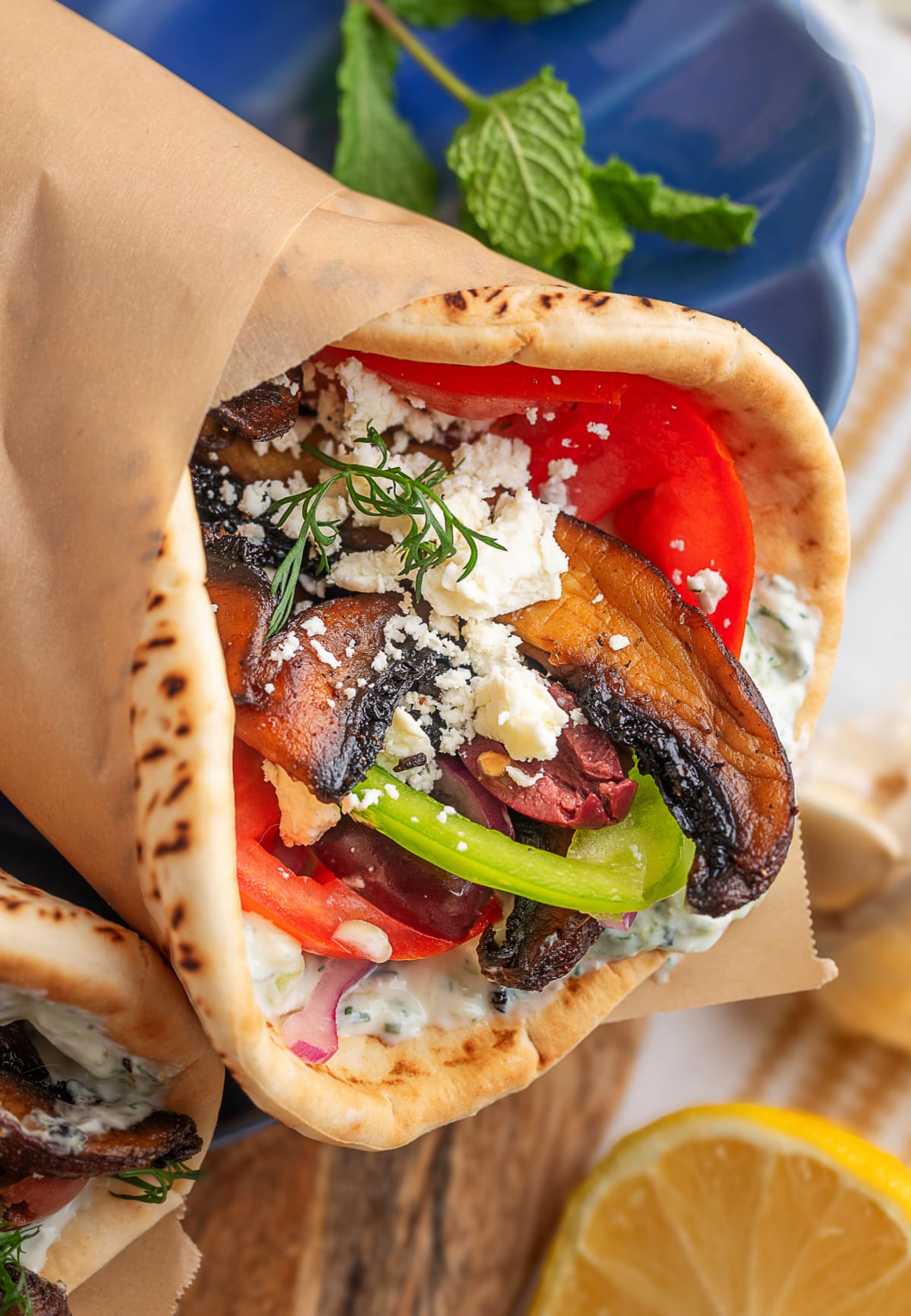 Close-up of portobello gyro in parchment wrap Close-up of one gyro wrapped in parchment with fillings visible.