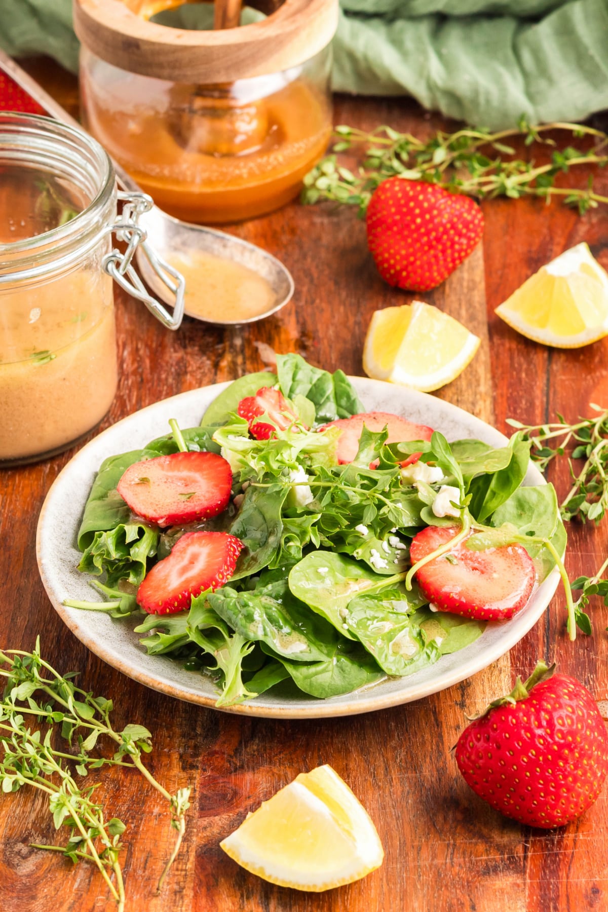 Fresh strawberry spinach salad drizzled with honey Dijon dressing, surrounded by dressing ingredients