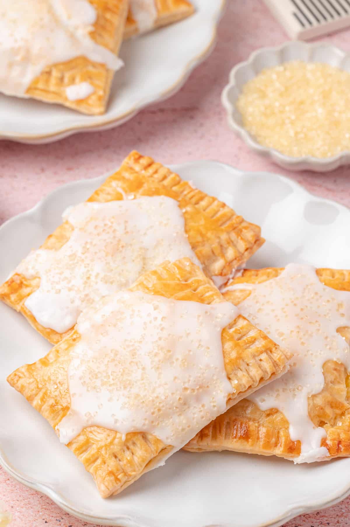 Close-up of glazed lemon pop tarts stacked on a white plate with coarse sugar on top 