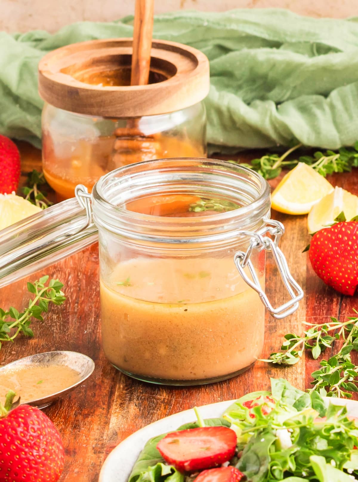 Fresh strawberry spinach salad drizzled with honey Dijon dressing, surrounded by dressing ingredients