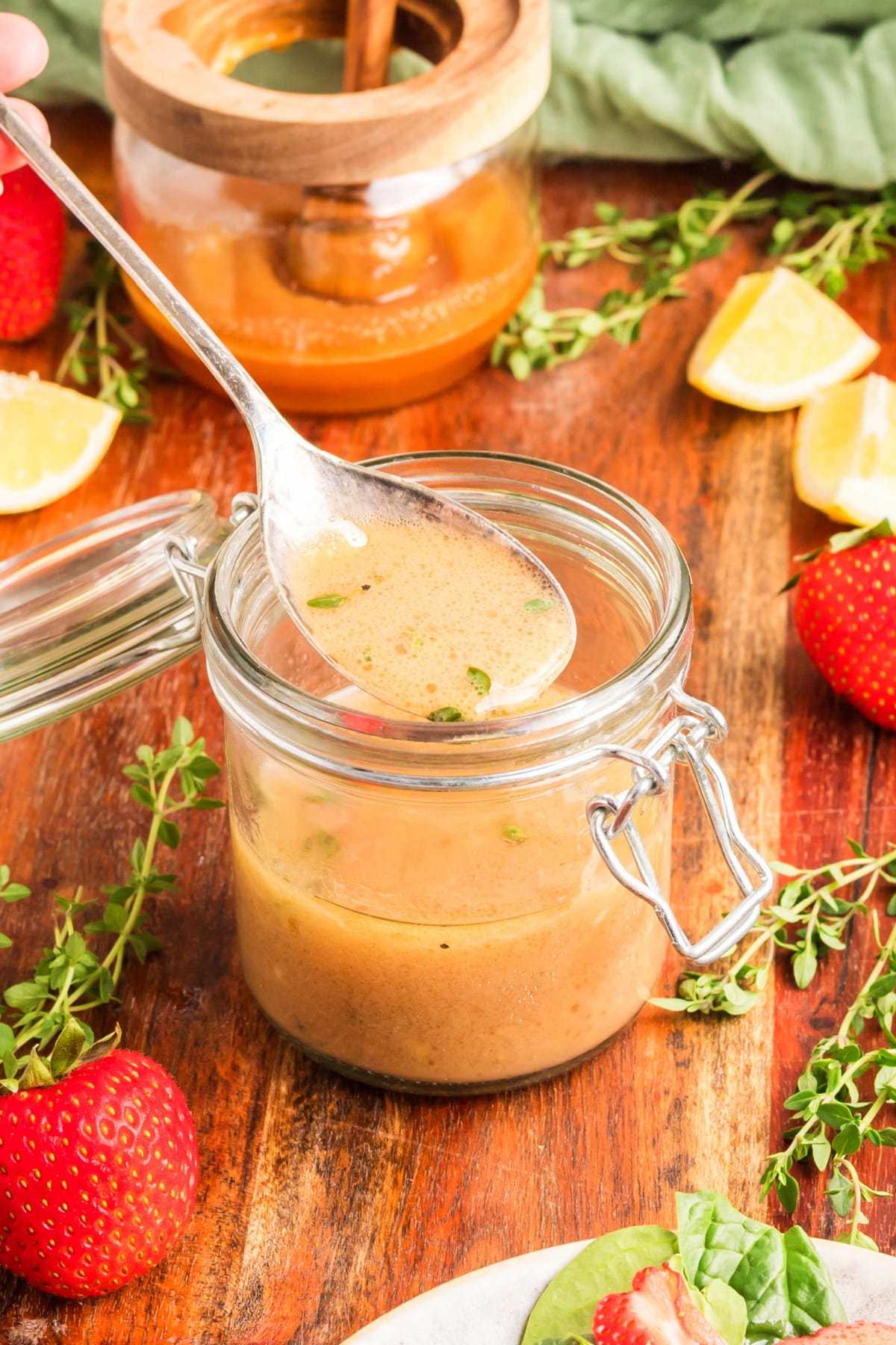 Spoon dipped into a jar of honey Dijon salad dressing with visible fresh thyme