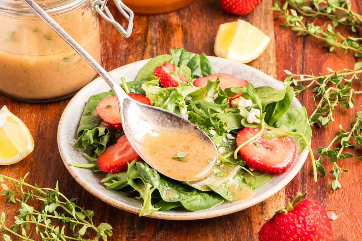 Spoon pouring honey Dijon dressing over a fresh spinach and strawberry salad