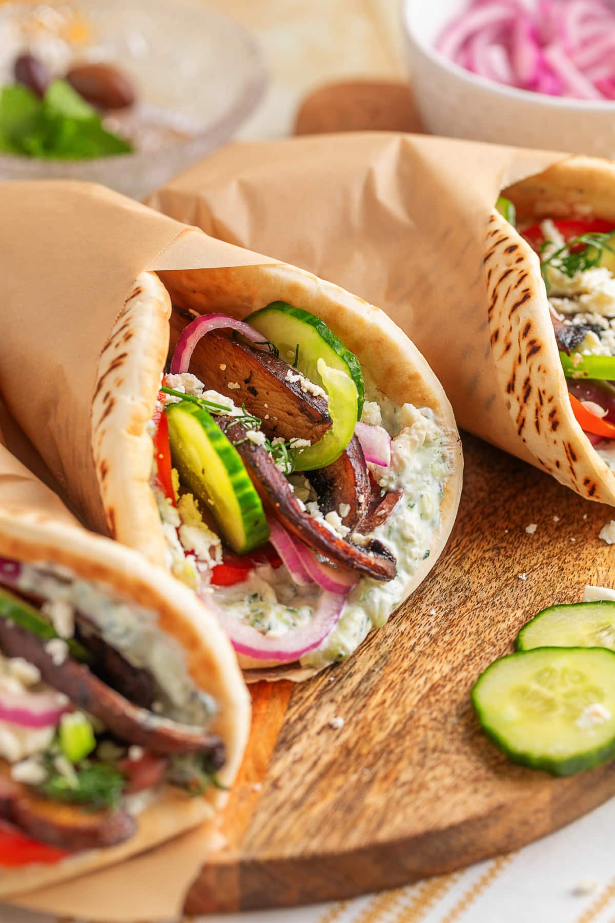 Finished portobello gyros wrapped in parchment paper Three assembled portobello mushroom gyros wrapped in parchment, ready to serve.