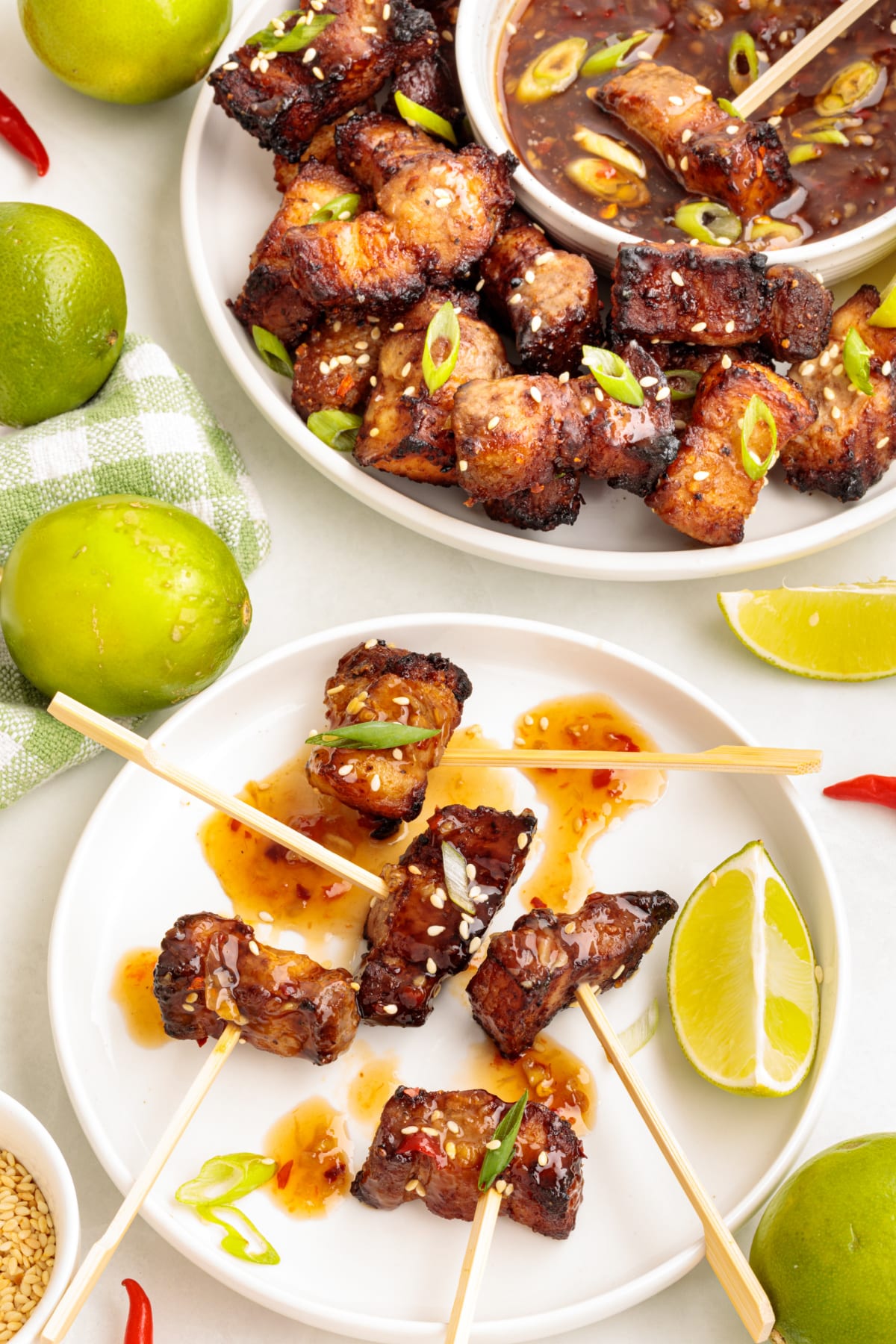 Plated air fryer pork belly bites with sweet chili lime dip, garnished with green onions and sesame seeds, served with limes and skewers.