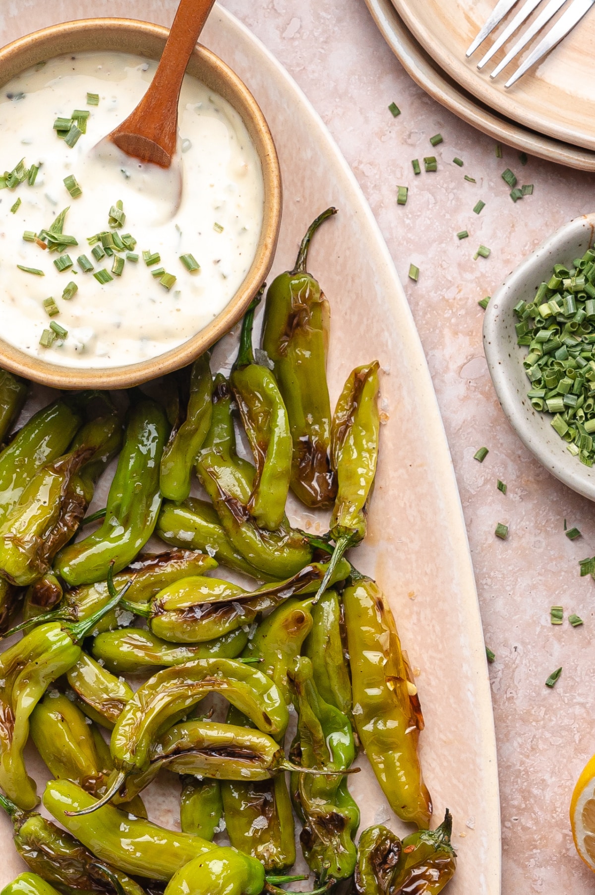 Blistered shishito peppers with aioli ready for dipping Blistered shishito peppers on a serving platter with a bowl of garlic chive aioli