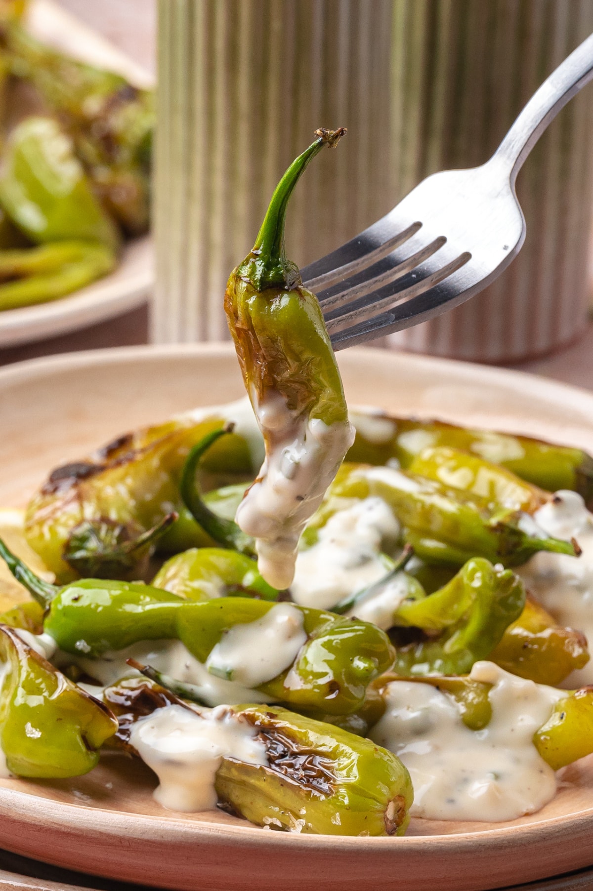 Dipping blistered shishito pepper in garlic chive sauce Fork lifting a blistered shishito pepper covered in creamy aioli