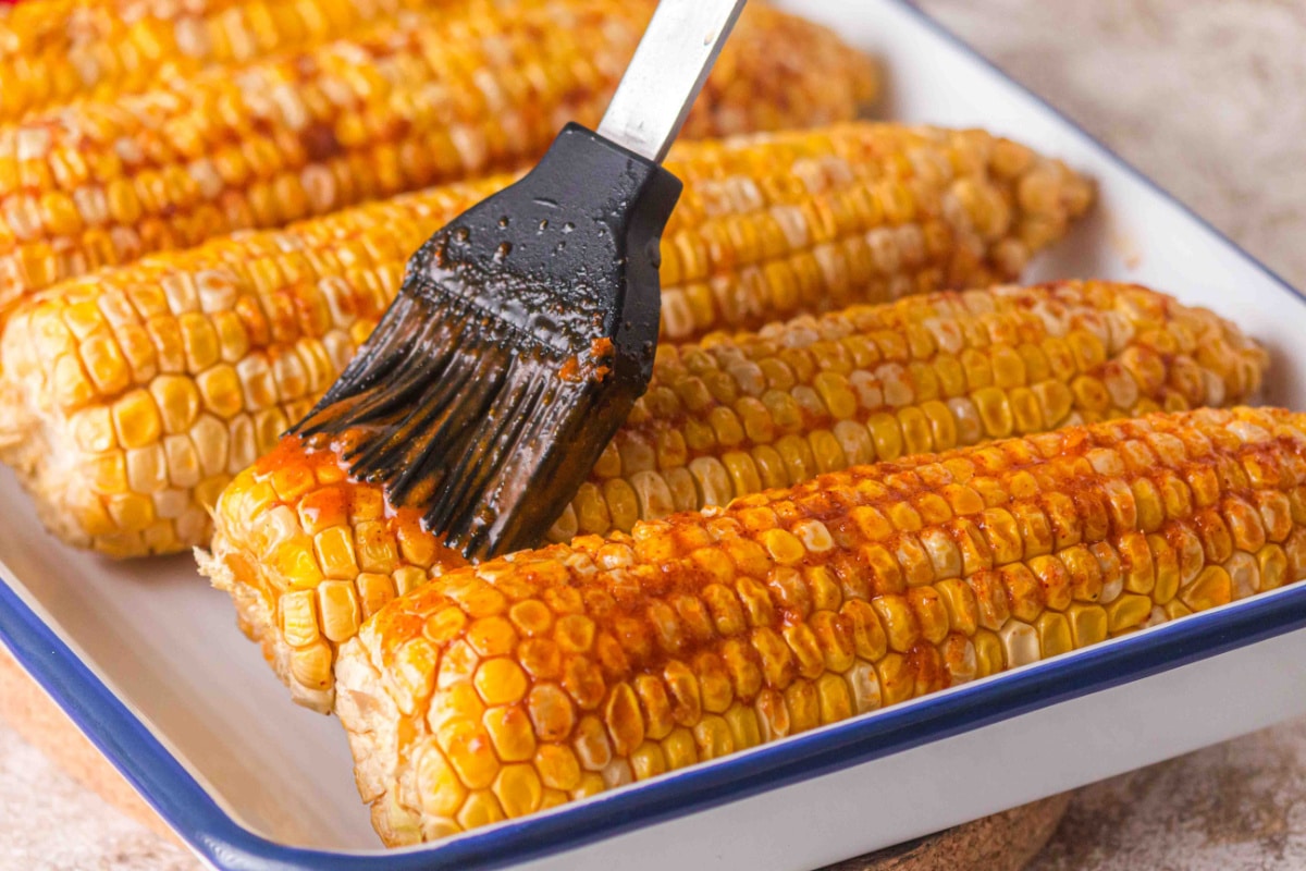 Smoked corn on the cob brushed with seasoned butter mixture on pellet grill Brushing garlic butter on smoked corn on the cob with brown sugar and paprika
