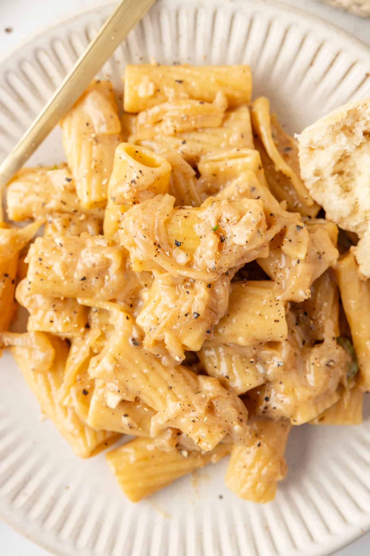French onion pasta with caramelized onions and Gruyere cheese on plate Creamy rigatoni pasta coated in caramelized onion sauce, served with cracked black pepper on a white plate.