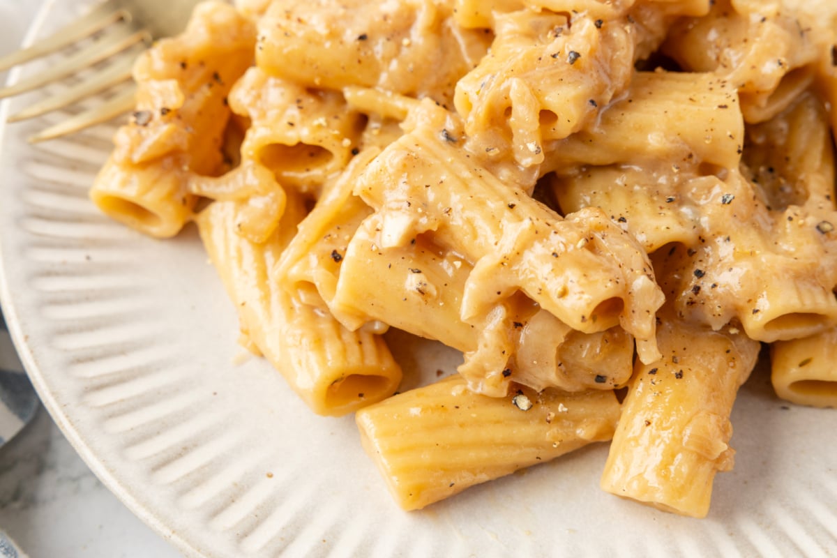 One-pan creamy French onion pasta with Gruyere Close-up of rigatoni in creamy French onion sauce with visible onion strands and melted cheese.