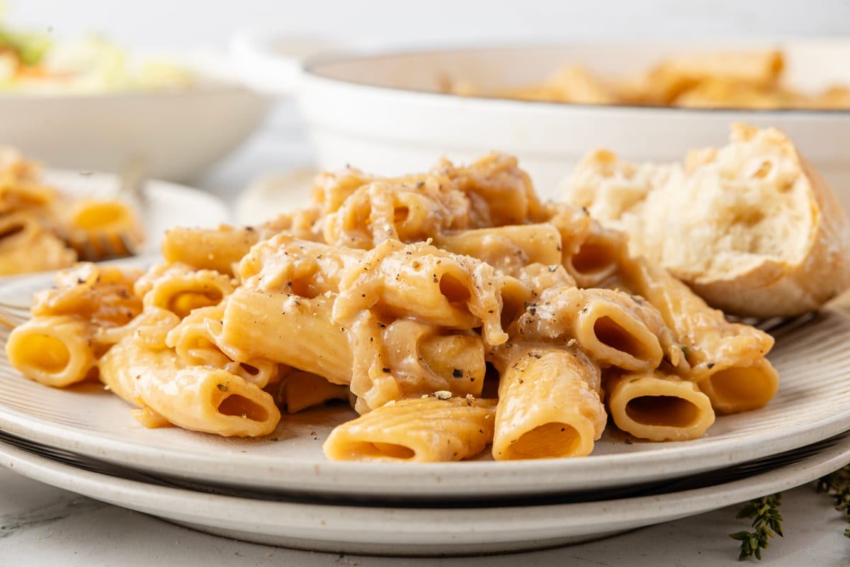Easy French onion rigatoni pasta served with bread Plated French onion pasta on a dinner plate with creamy sauce and a piece of bread.