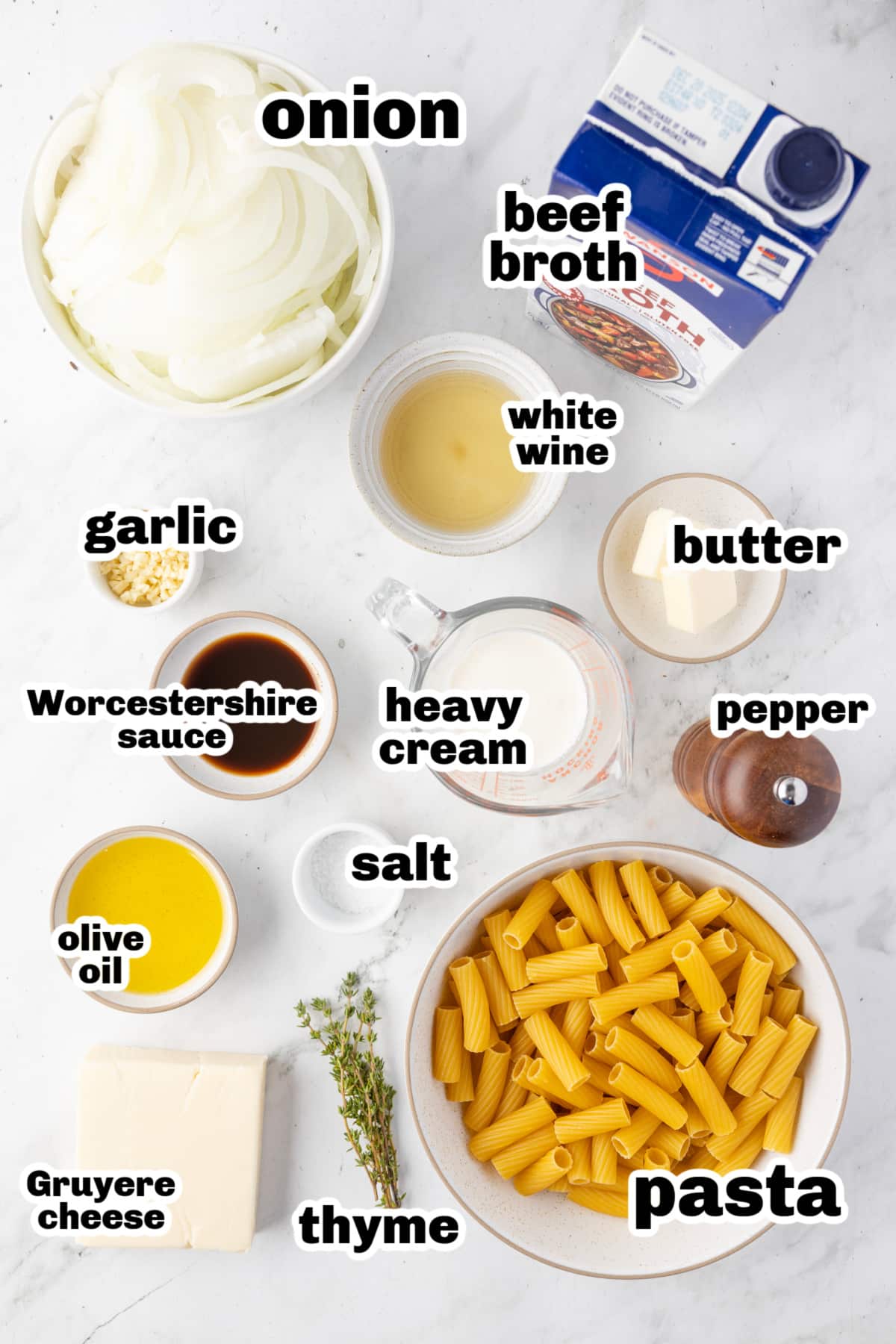 Ingredients laid out for French onion rigatoni pasta recipe Overhead shot of ingredients for French onion pasta, including onions, broth, pasta, cheese, and herbs.