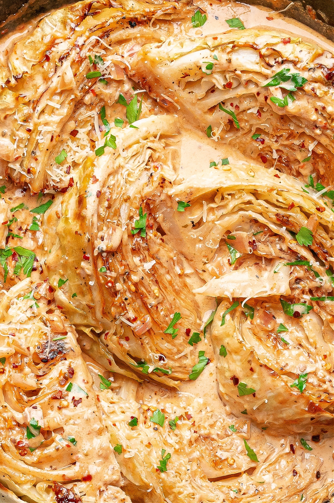 Creamy melting cabbage wedges in a Tuscan-style sauce with sun-dried tomatoes and herbs, garnished with parsley and Parmesan.