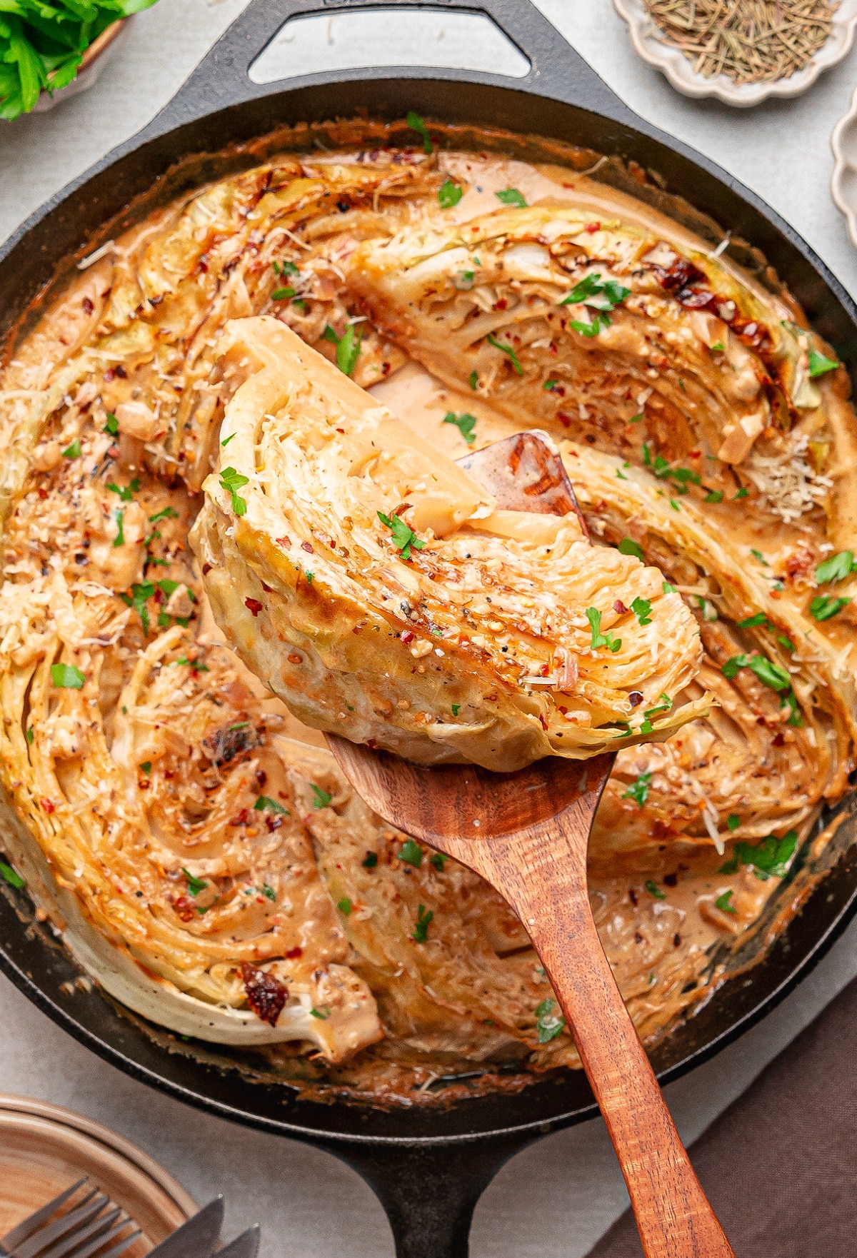 One pan Tuscan cabbage recipe with a golden caramelized wedge being lifted from creamy sauce in a cast iron skillet.