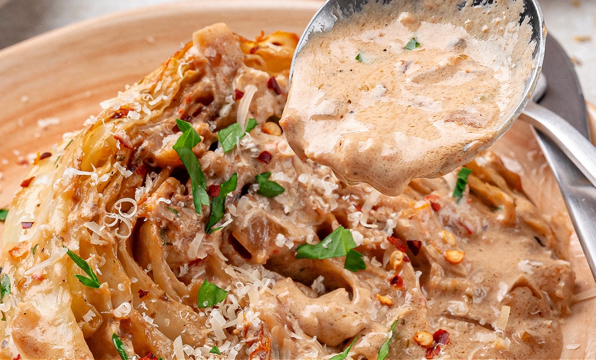Close-up of creamy Tuscan cabbage sauce being spooned over soft cabbage wedges, topped with Parmesan and herbs.