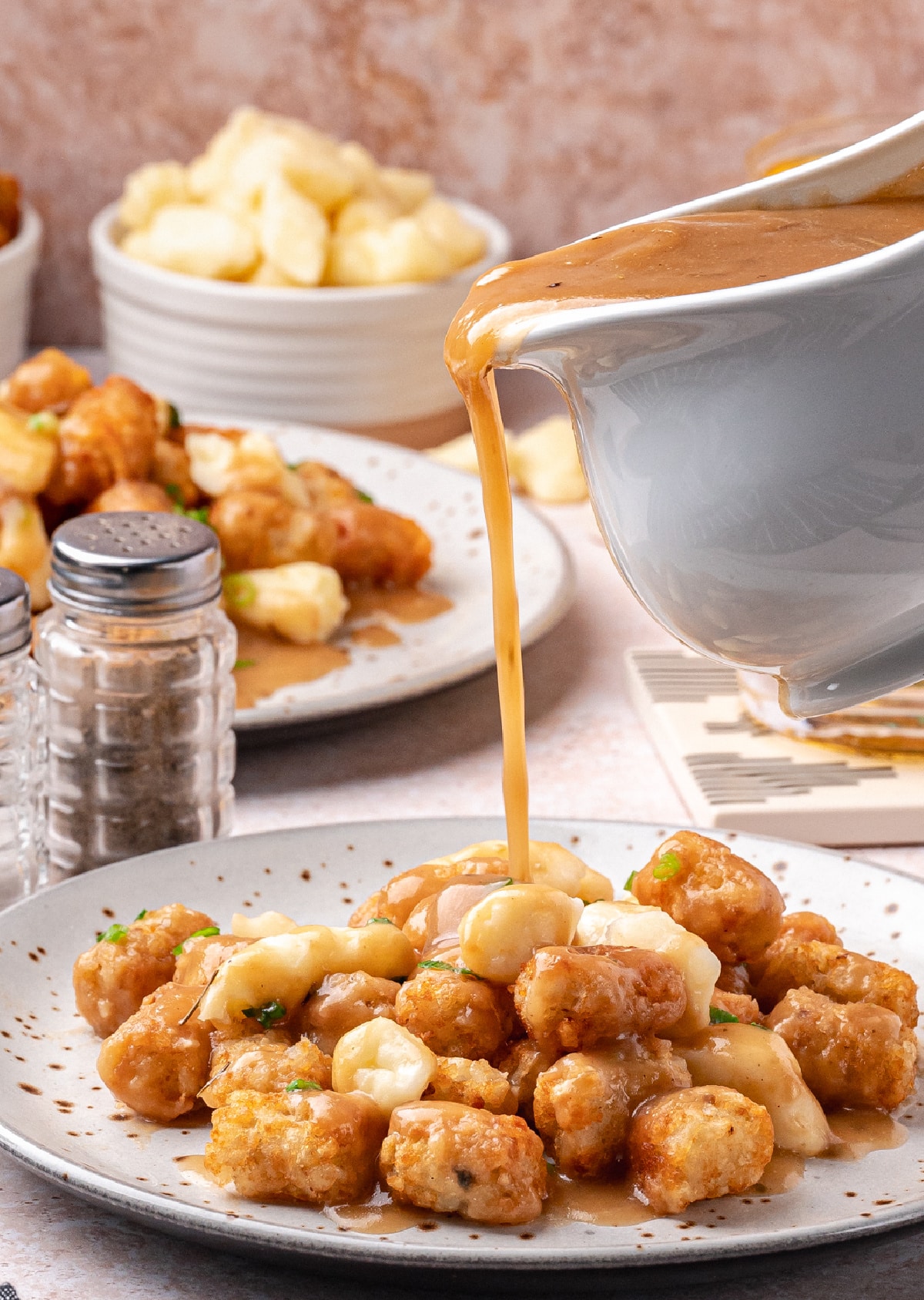Pouring Gravy Over Cheese Curd Tater Tot Poutine Gravy being poured over crispy tater tots and cheese curds to assemble homemade tater tot poutine.