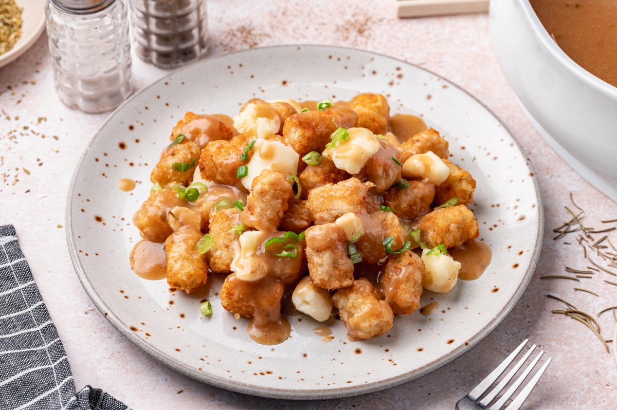 Homemade Tater Tot Poutine with Cheese Curds and Brown Gravy Plate of homemade tater tot poutine topped with melty cheese curds, rich brown gravy, and green onions.