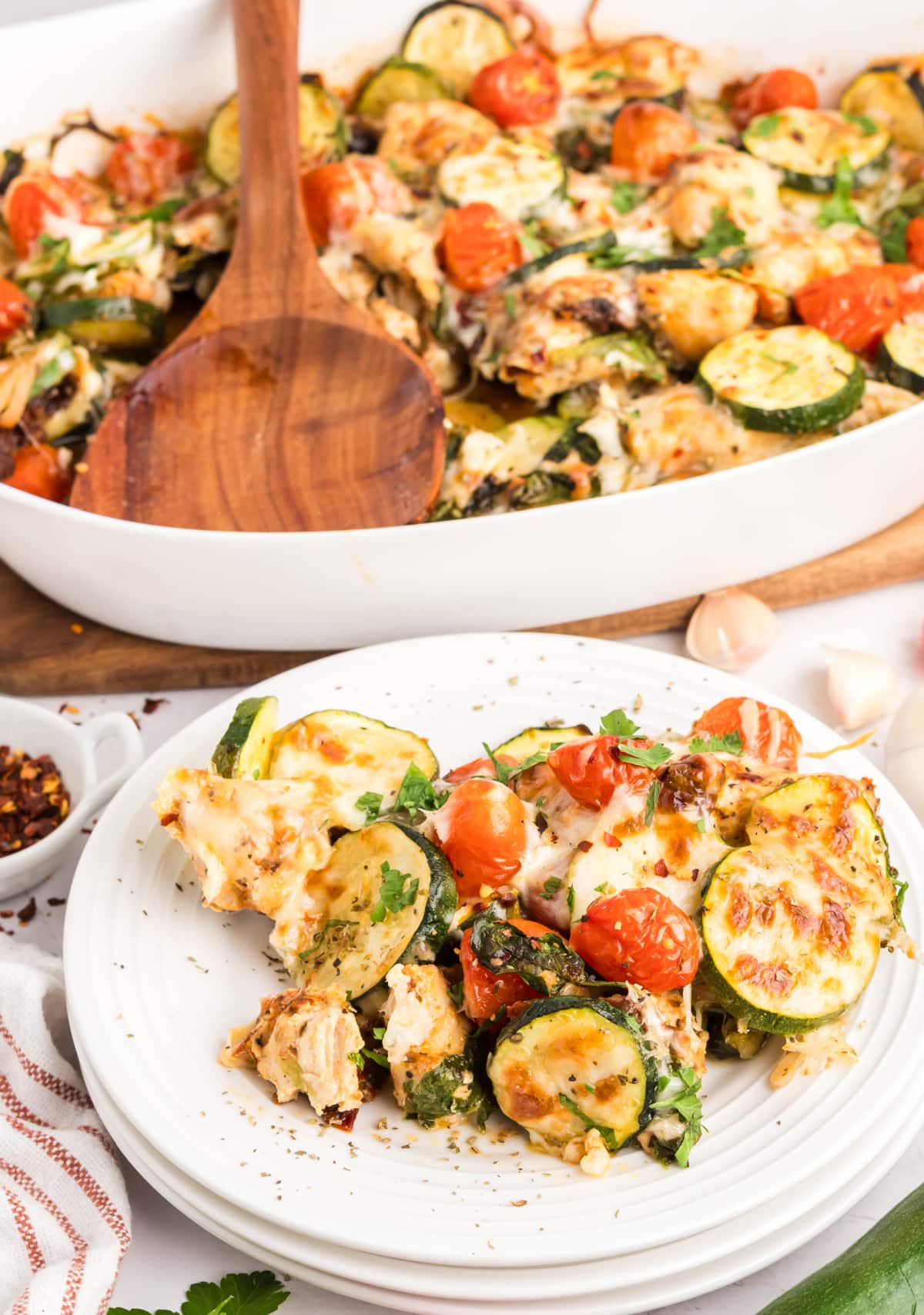 Chicken Zucchini Casserole with Tomatoes and Herbs Serving of baked chicken zucchini casserole on white plate with fresh herbs and visible browned cheese.