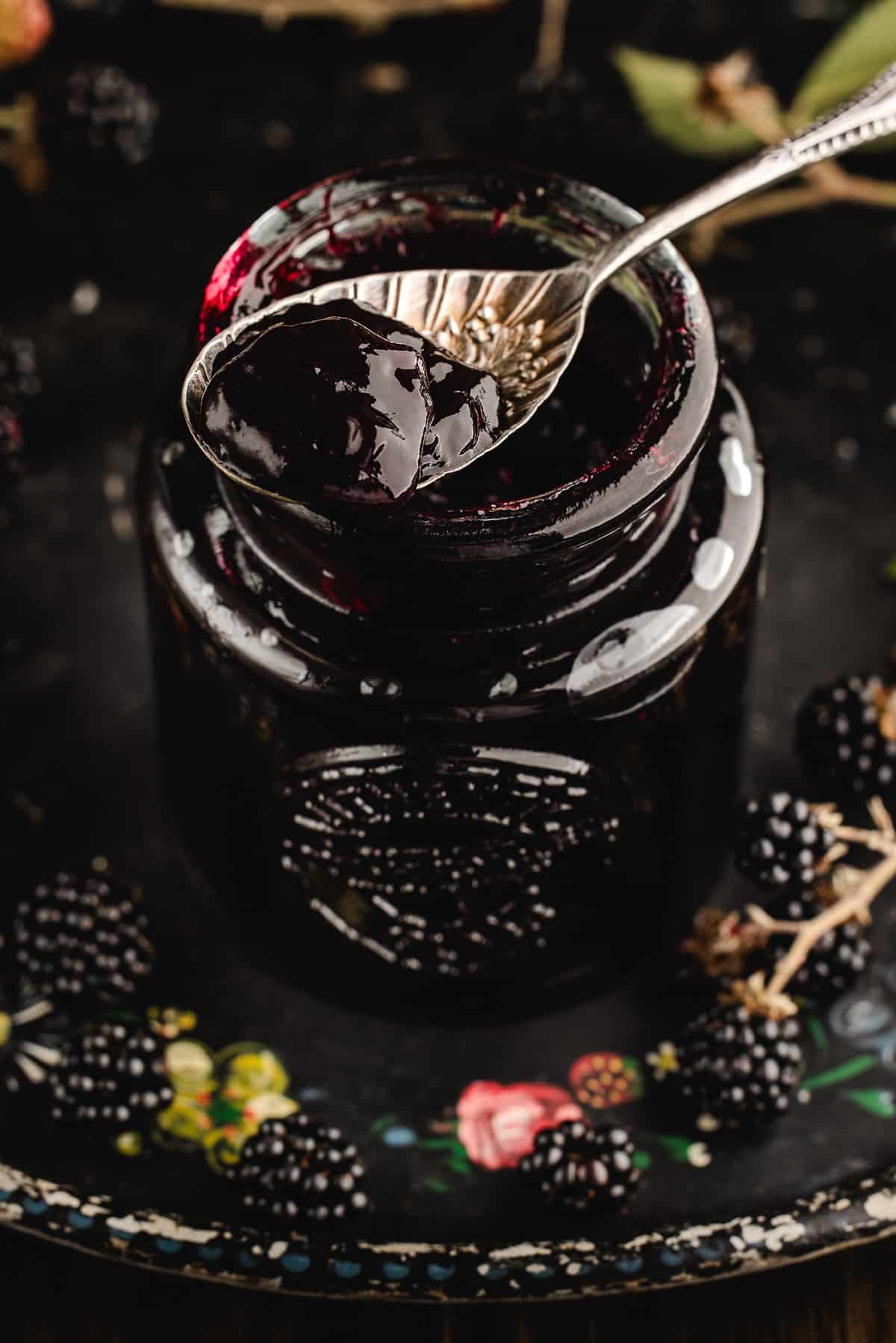 Vintage spoon dipped into a jar of glossy jam on a floral tray with berries