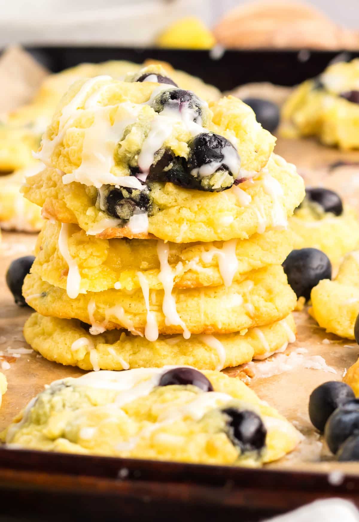 Lemon Blueberry Cookies with Glaze Drizzle Stack of soft lemon blueberry cookies with glaze and fresh blueberries on parchment