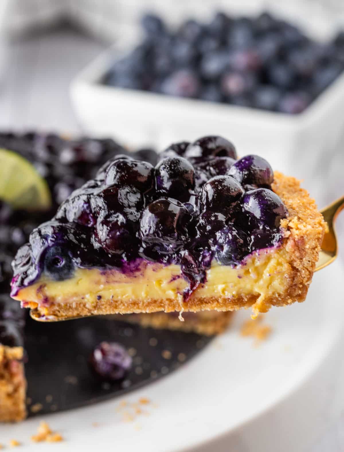 Blueberry Key Lime Tart slice on server. Blueberry Key Lime Tart slice lifted from pan showing custard and blueberry topping.