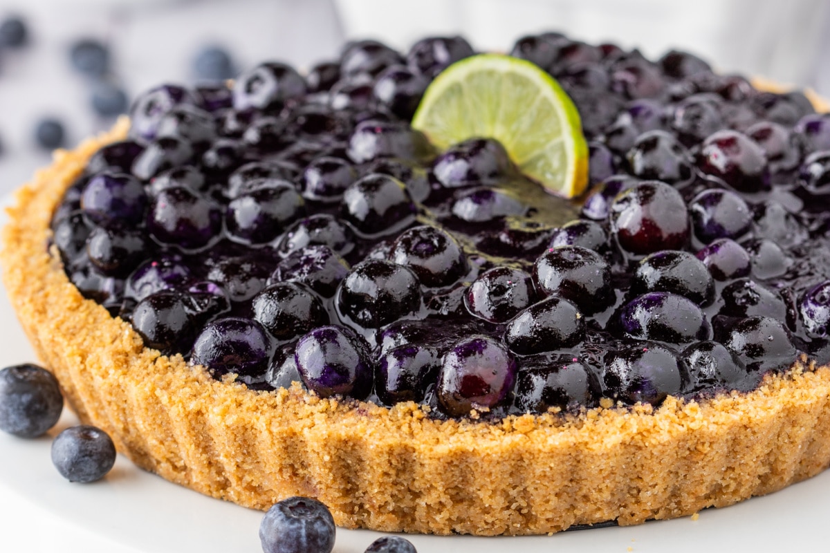 Blueberry Key Lime Tart whole with garnish. Blueberry Key Lime Tart in tart pan topped with lime wedge and fresh blueberries.