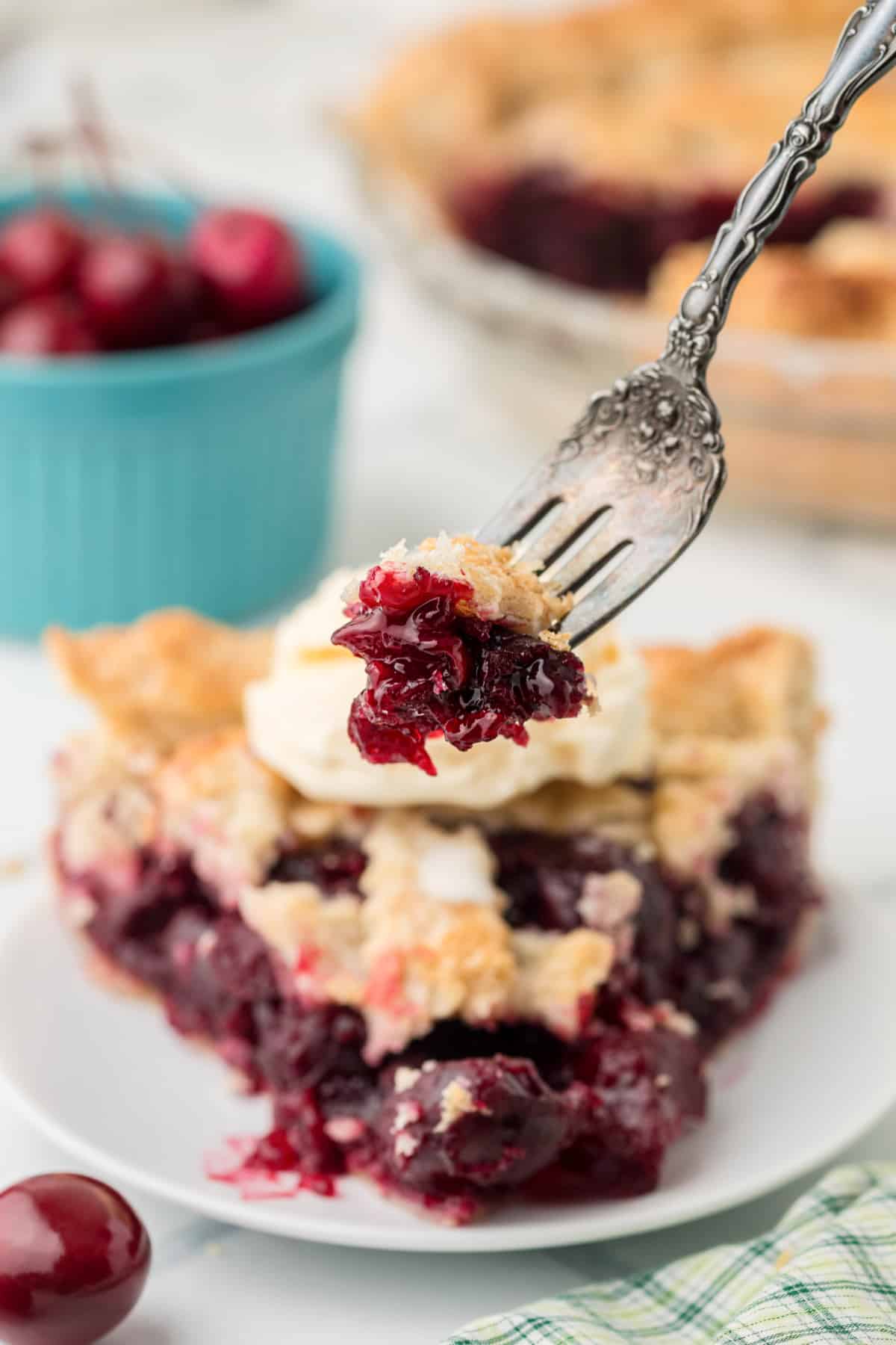 Forkful of Fresh Cherry Pie showing thick cherry filling with a slice in the background