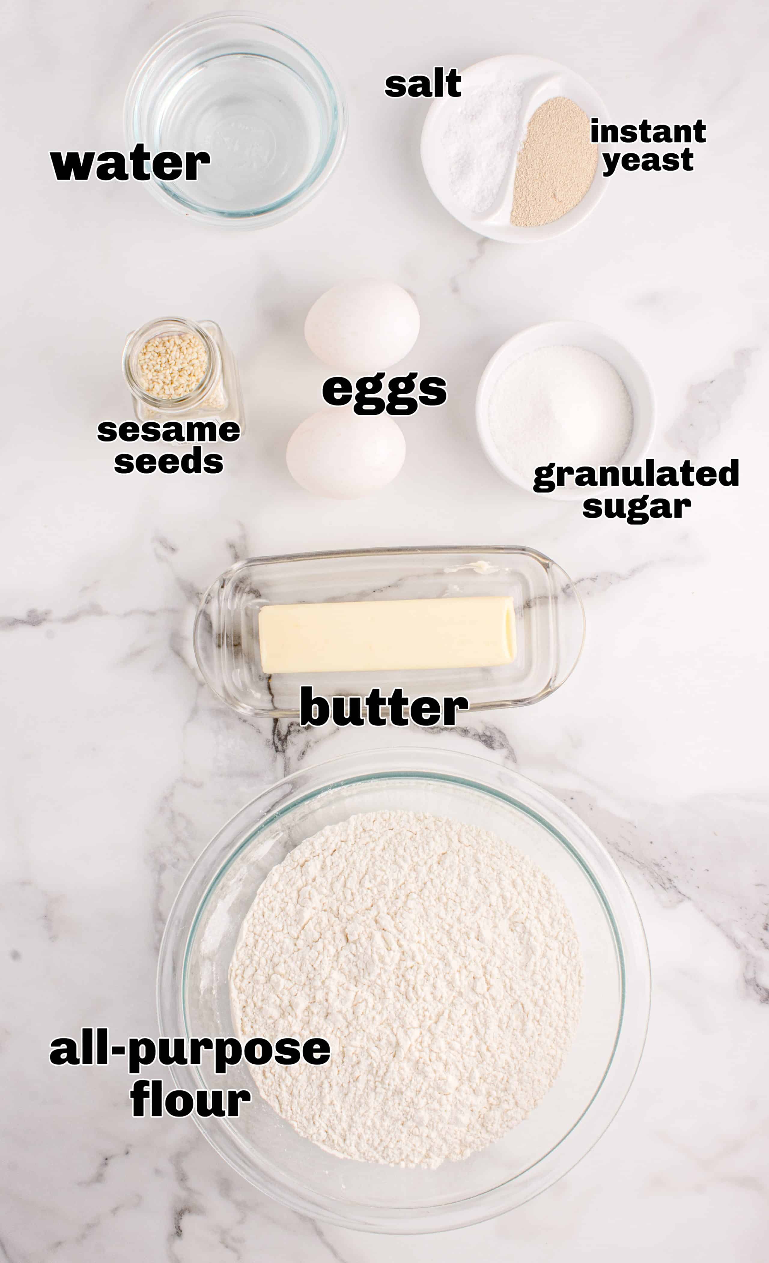 Slider bun ingredients measured and ready for baking Ingredients for making homemade slider buns including flour, yeast, eggs, butter, and sesame seeds