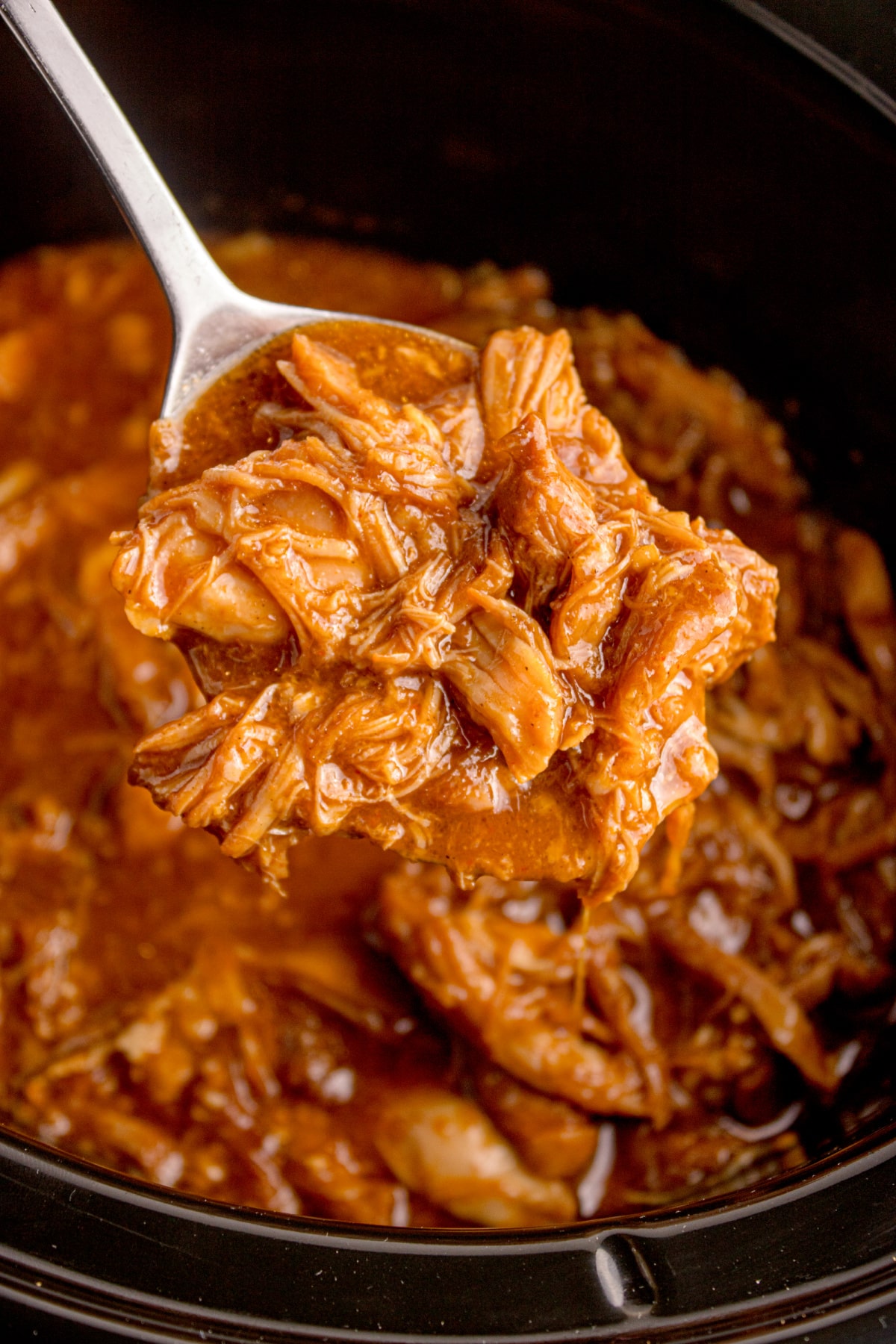 Close-up of shredded Korean BBQ chicken in a slow cooker, coated in glossy sauce.