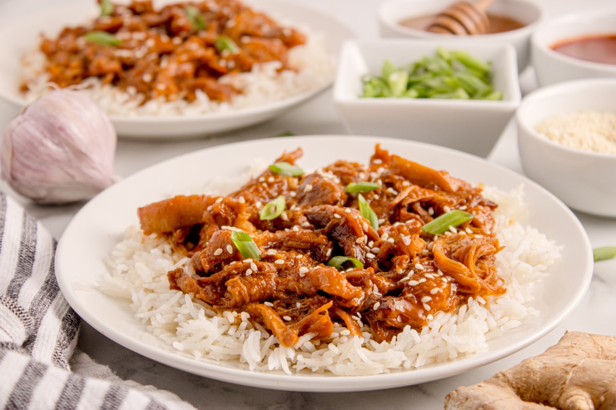 Plated Korean BBQ chicken on rice, garnished with sesame seeds and green onions.