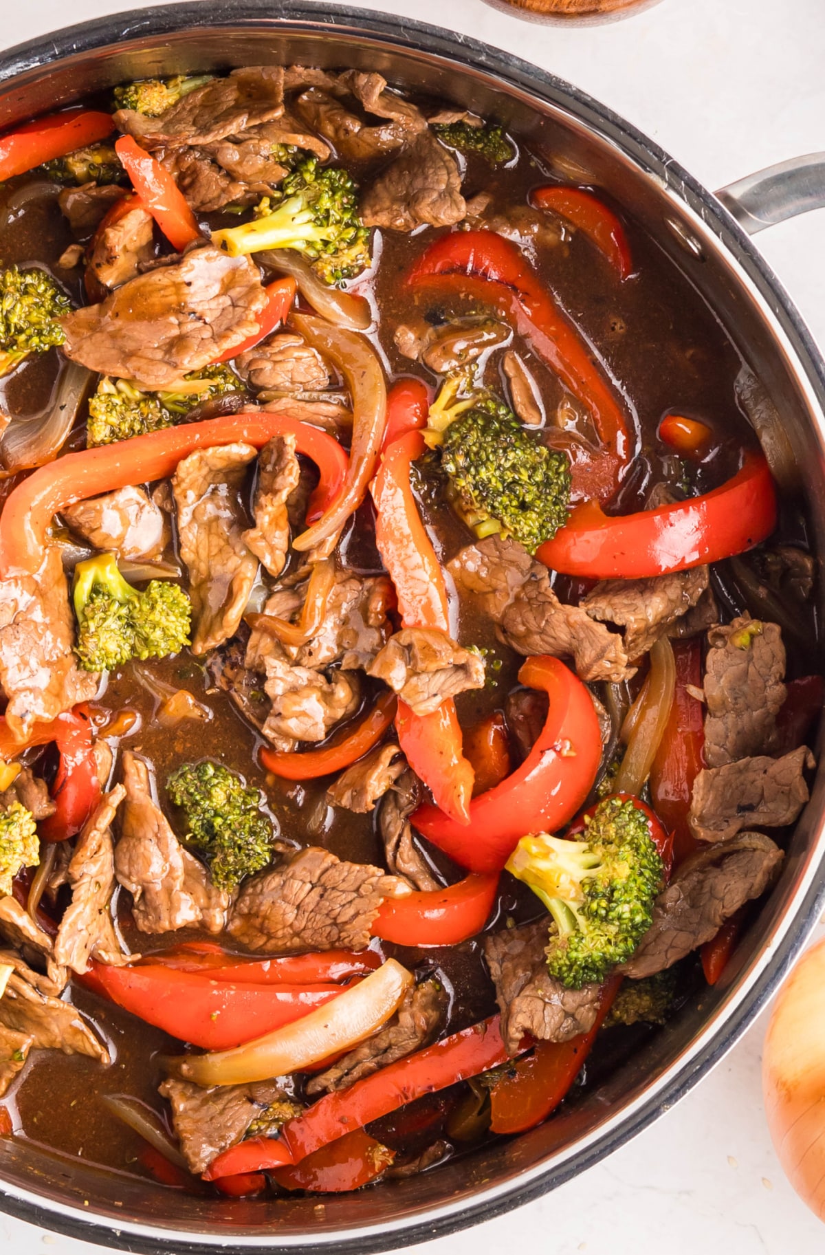 Beef, broccoli, and red peppers simmering in teriyaki sauce in a skillet