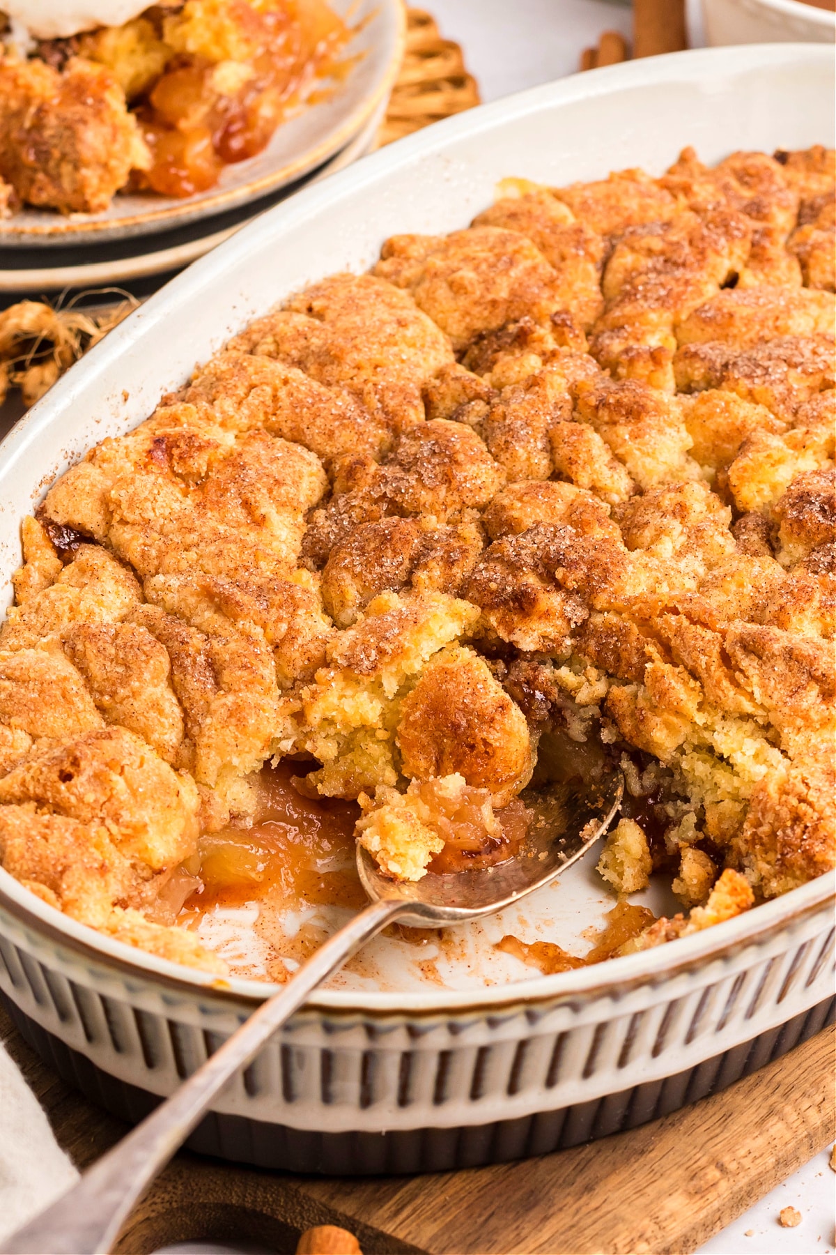 Baked snickerdoodle apple cobbler in white dish with a spoonful scooped out.