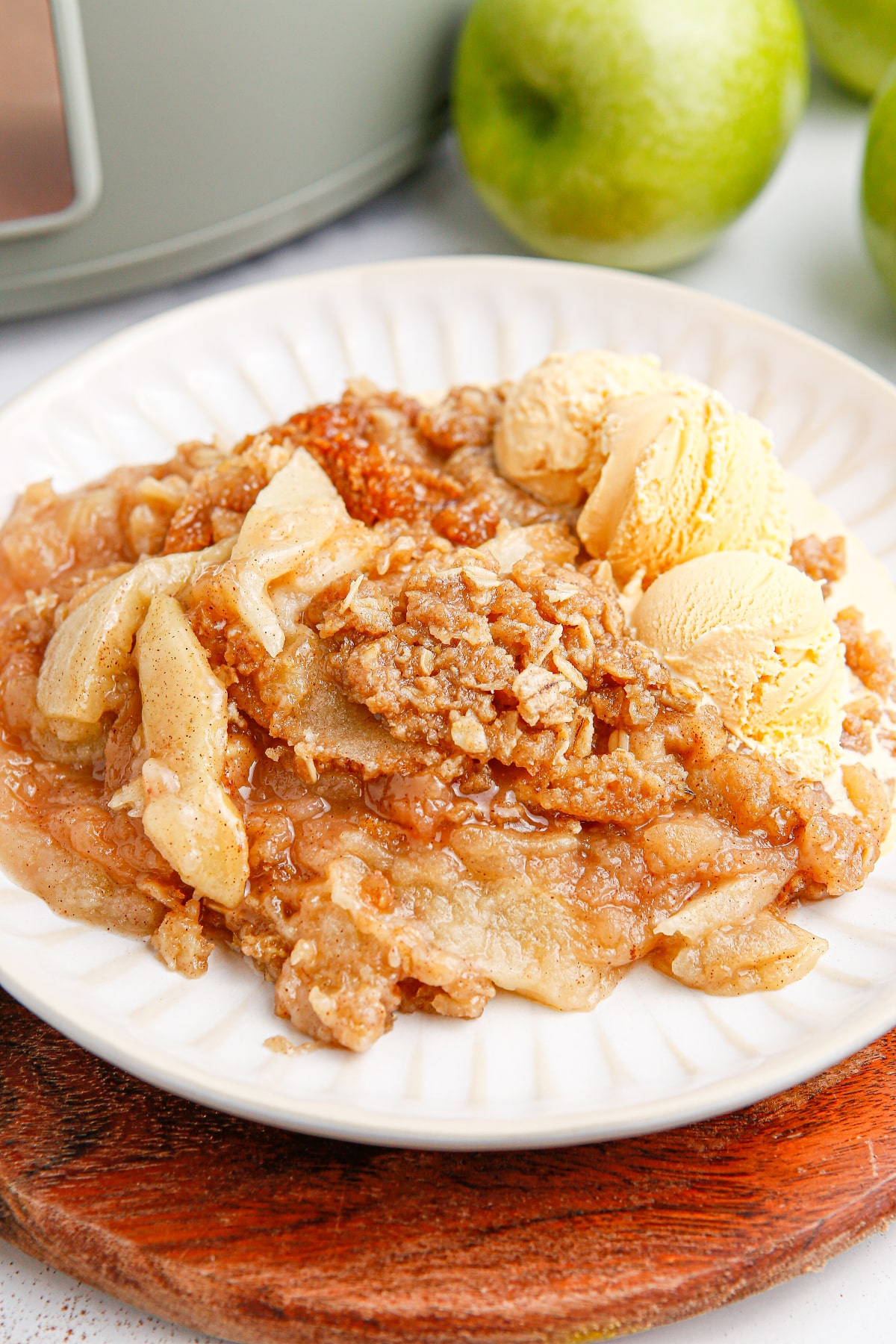 Close-up of crockpot apple crisp with tender apple slices, crisp oat topping, and vanilla ice cream.