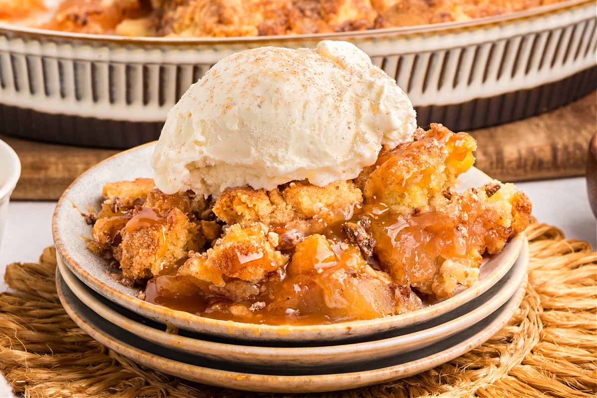 Plate of apple cobbler topped with vanilla ice cream and caramel sauce.