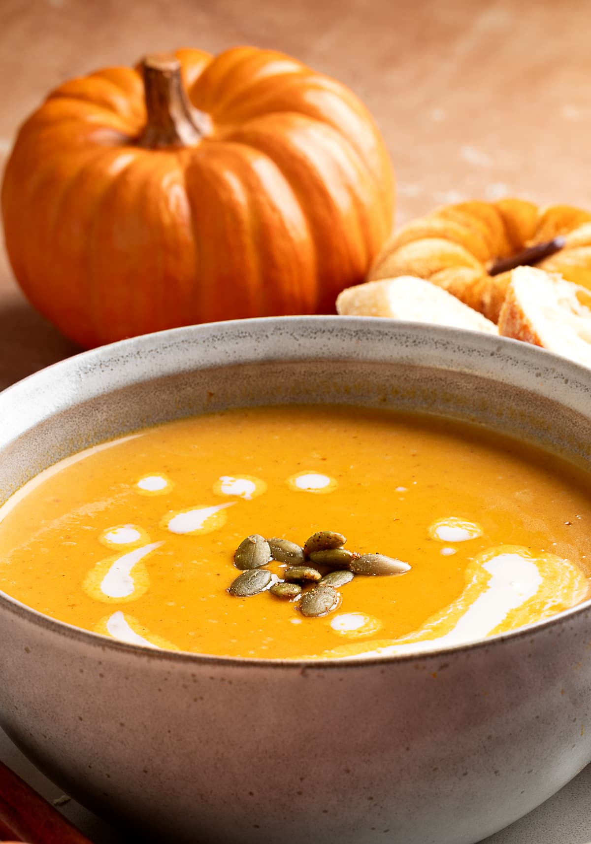bowl of pumpkin soup with cream and pepitas roasted garlic pumpkin soup with brown butter in a stoneware bowl, swirled with cream and topped with pumpkin seeds