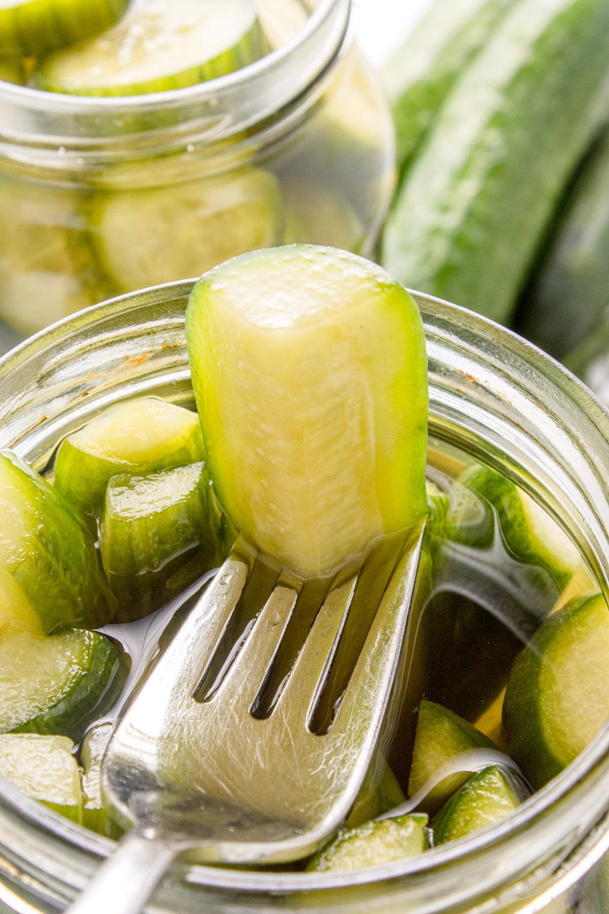 Fork lifting a crunchy slice of homemade dill pickle from the jar.
