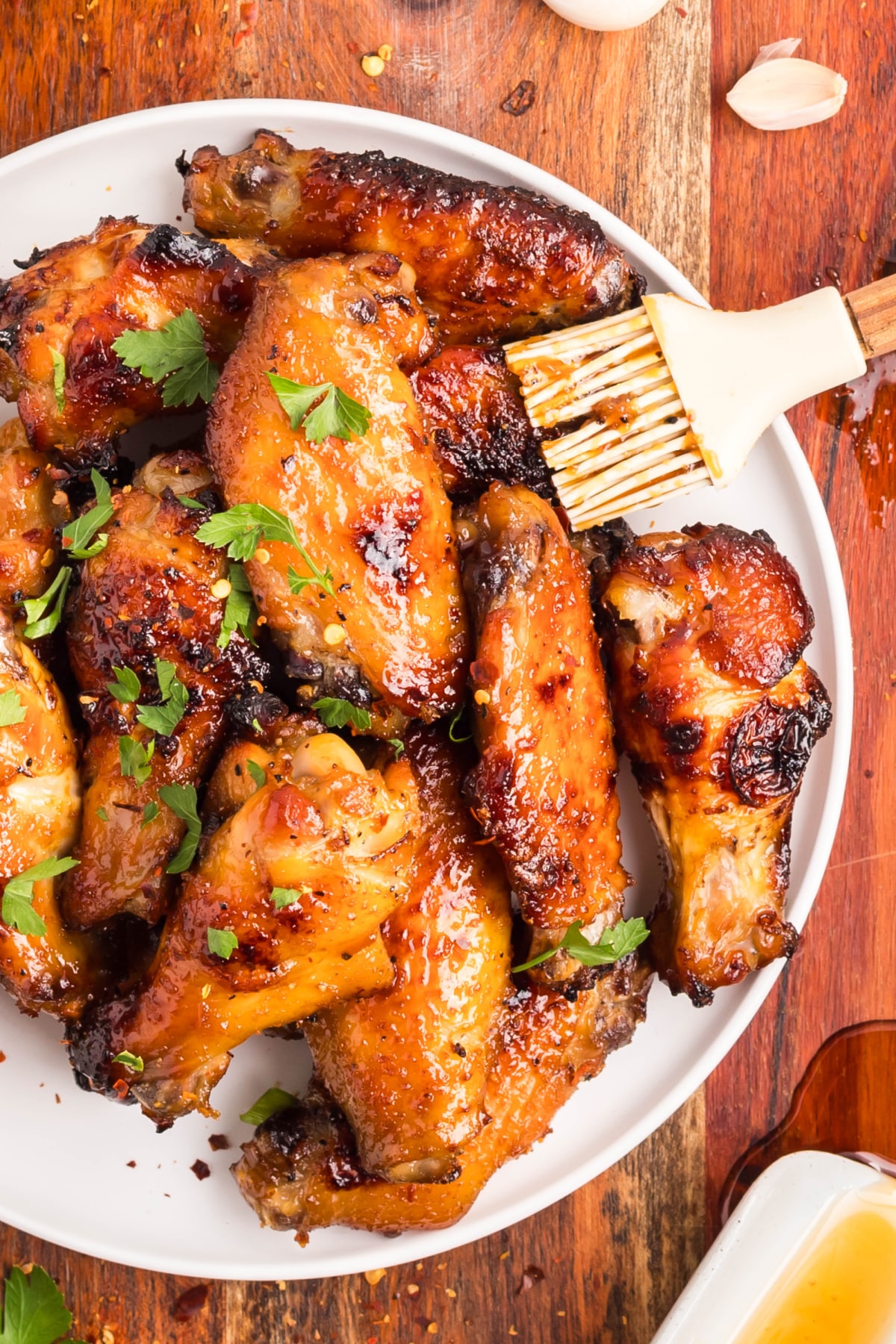 Baked honey garlic chicken wings with parsley garnish. Baked honey garlic chicken wings on a white plate with parsley and a brush of sticky sauce.