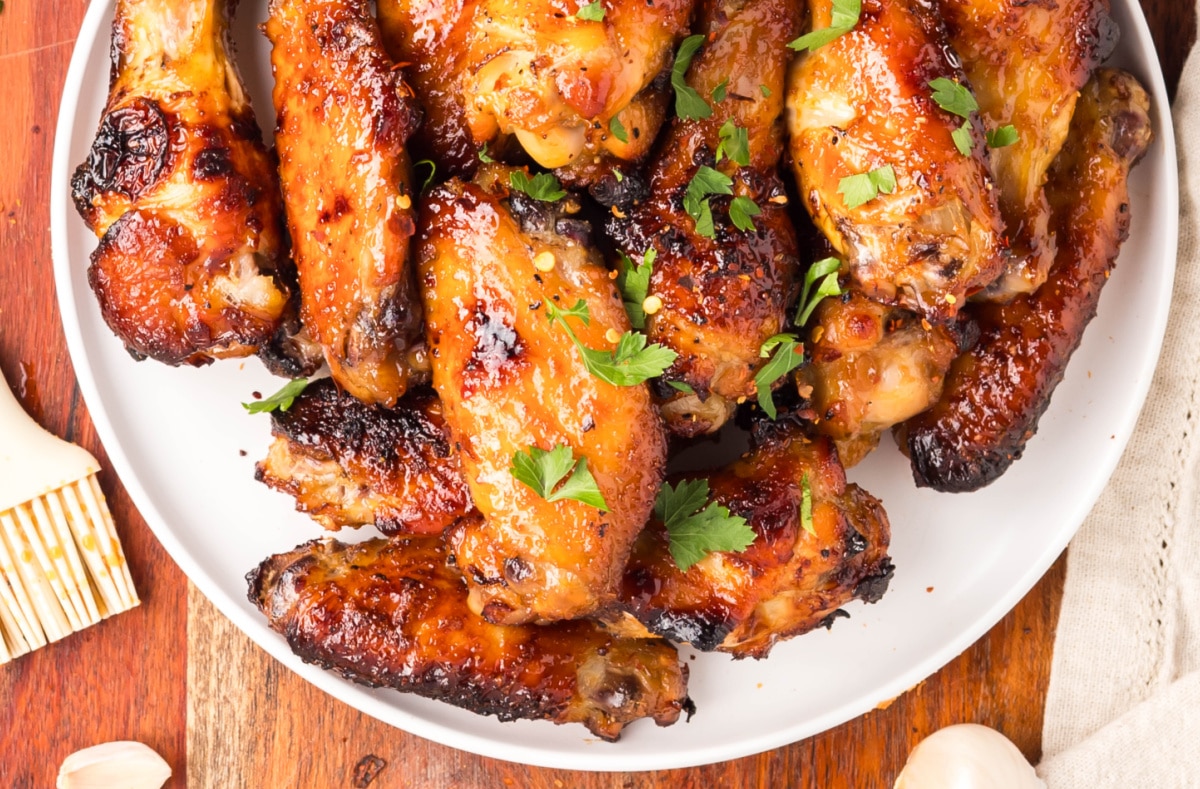 Crispy baked honey garlic chicken wingette with sauce. Crispy baked honey garlic chicken wingette held up close with parsley garnish.