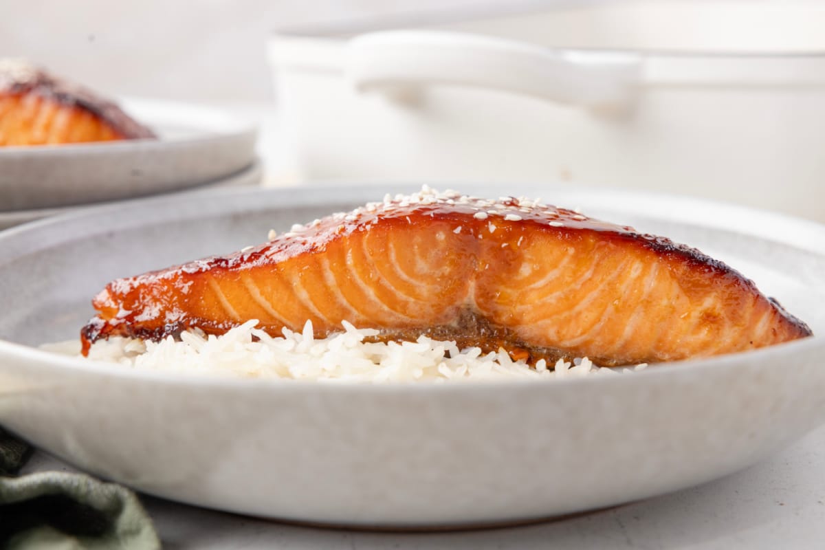Baked salmon fillet with miso glaze served over white rice in a shallow bowl.