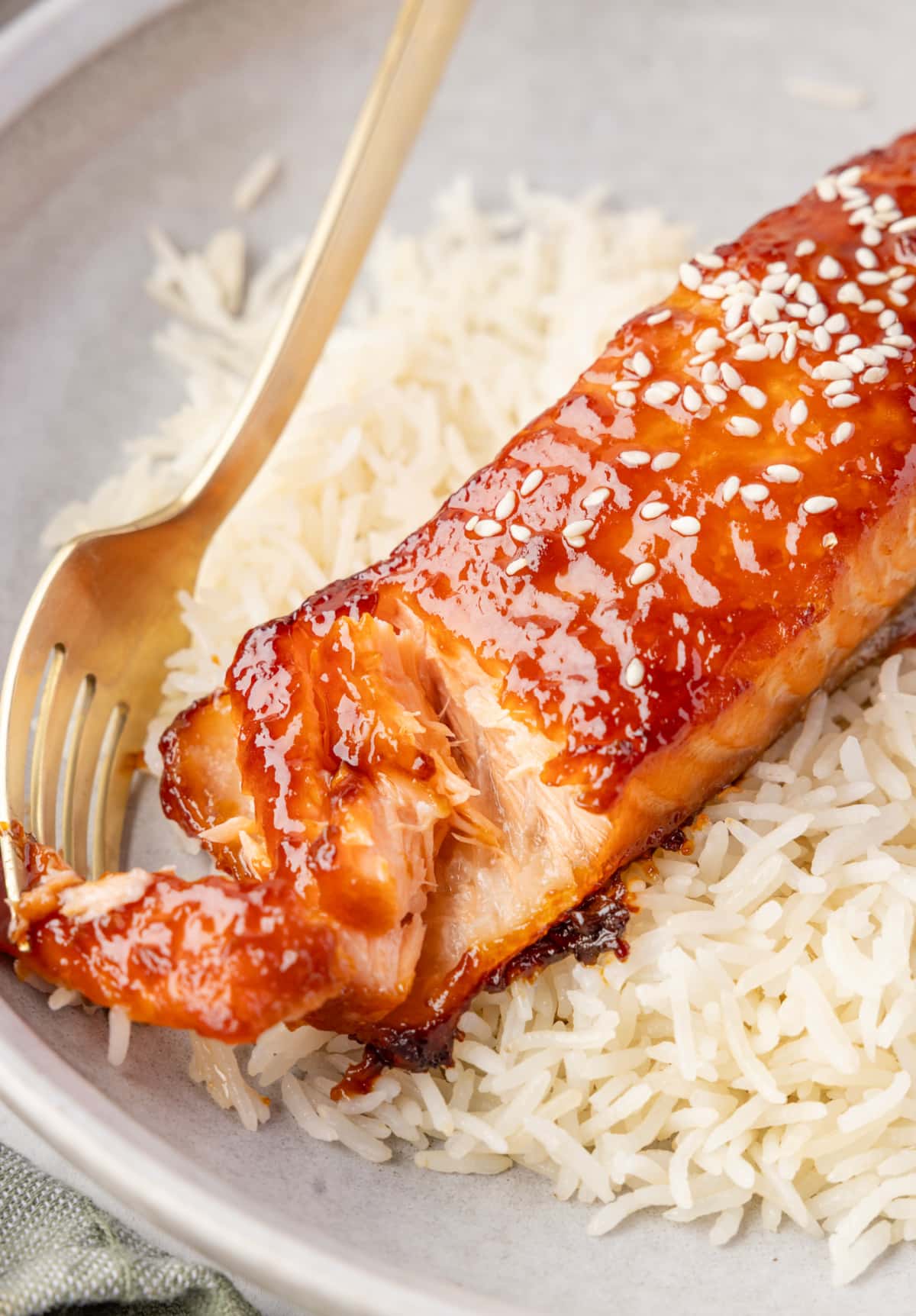 Miso salmon with sesame seeds, served over rice with a fork pulling a piece away.