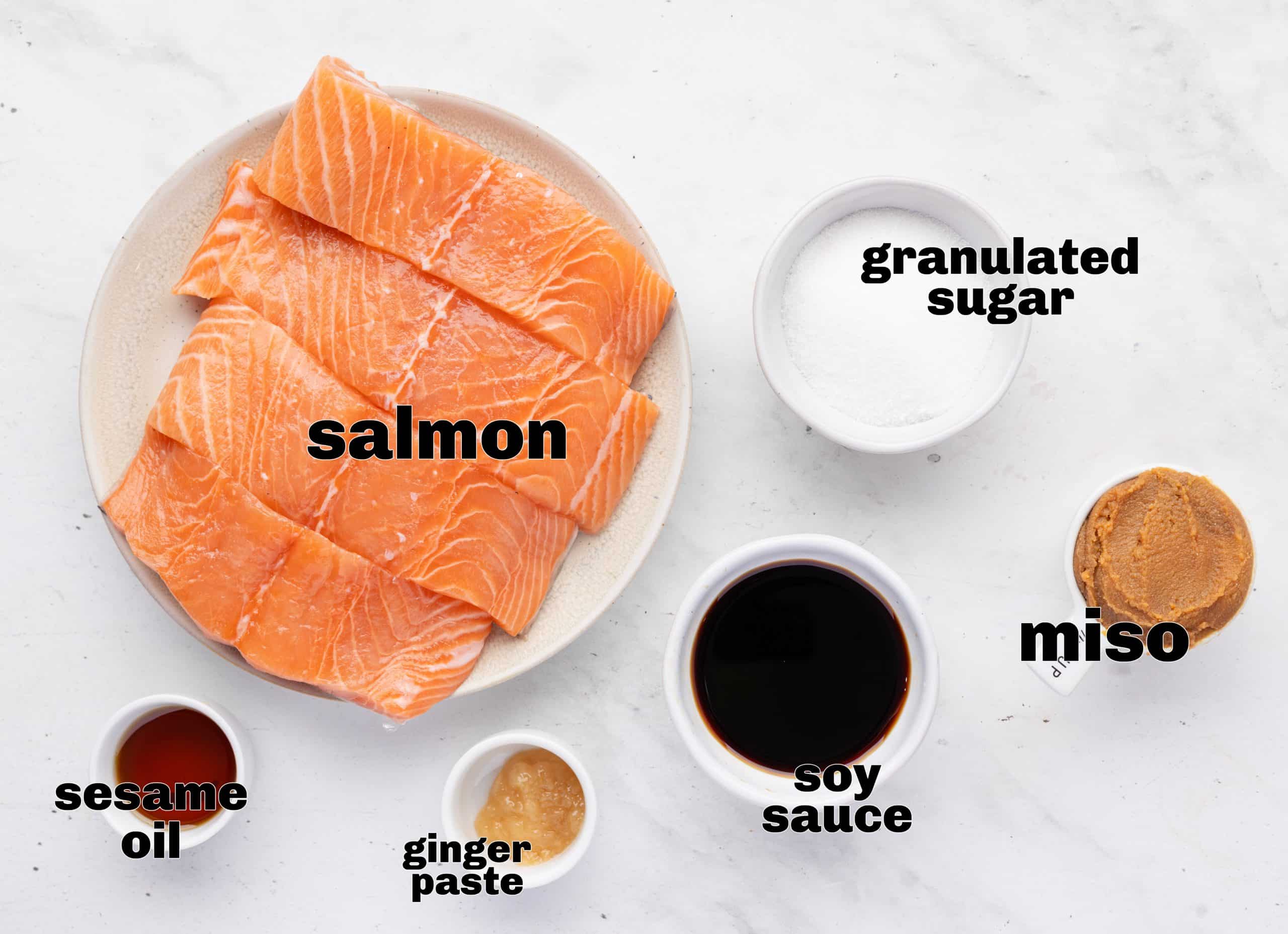 Ingredients for baked miso salmon including fresh salmon, miso paste, soy sauce, ginger, sesame oil, and sugar.