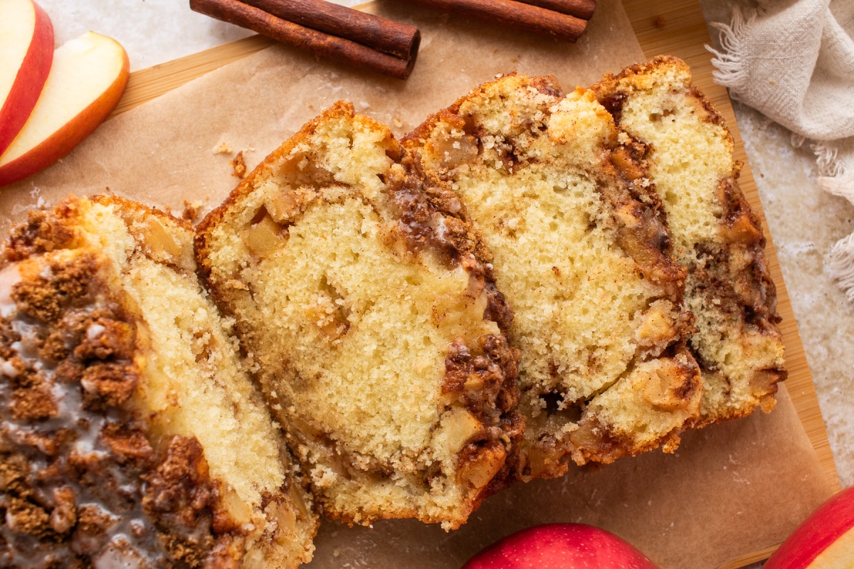 Cinnamon swirl apple bread sliced on parchment with fresh apples and cinnamon sticks.