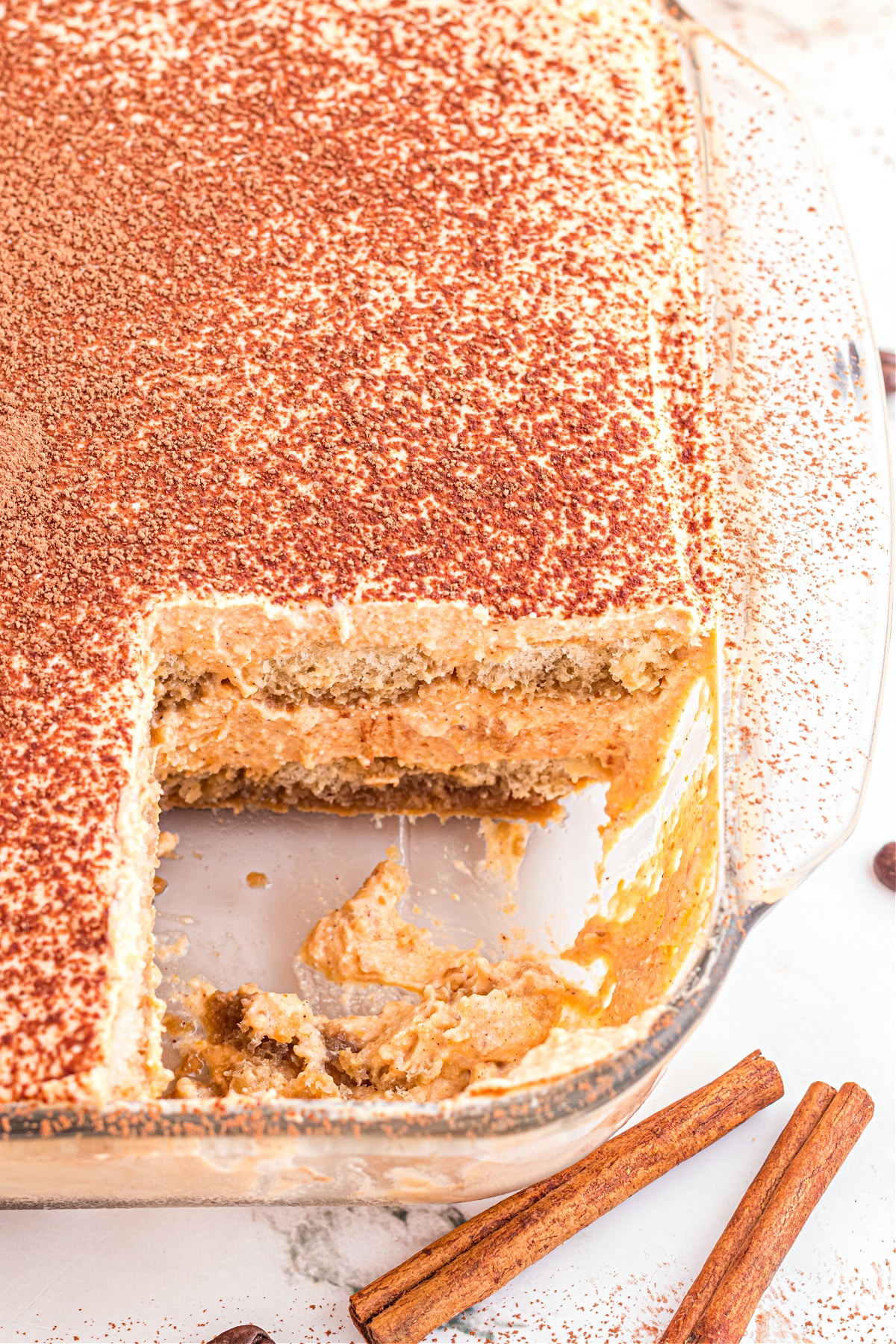 Simple pumpkin tiramisu in baking dish Pumpkin tiramisu in glass dish with slice removed showing creamy layers