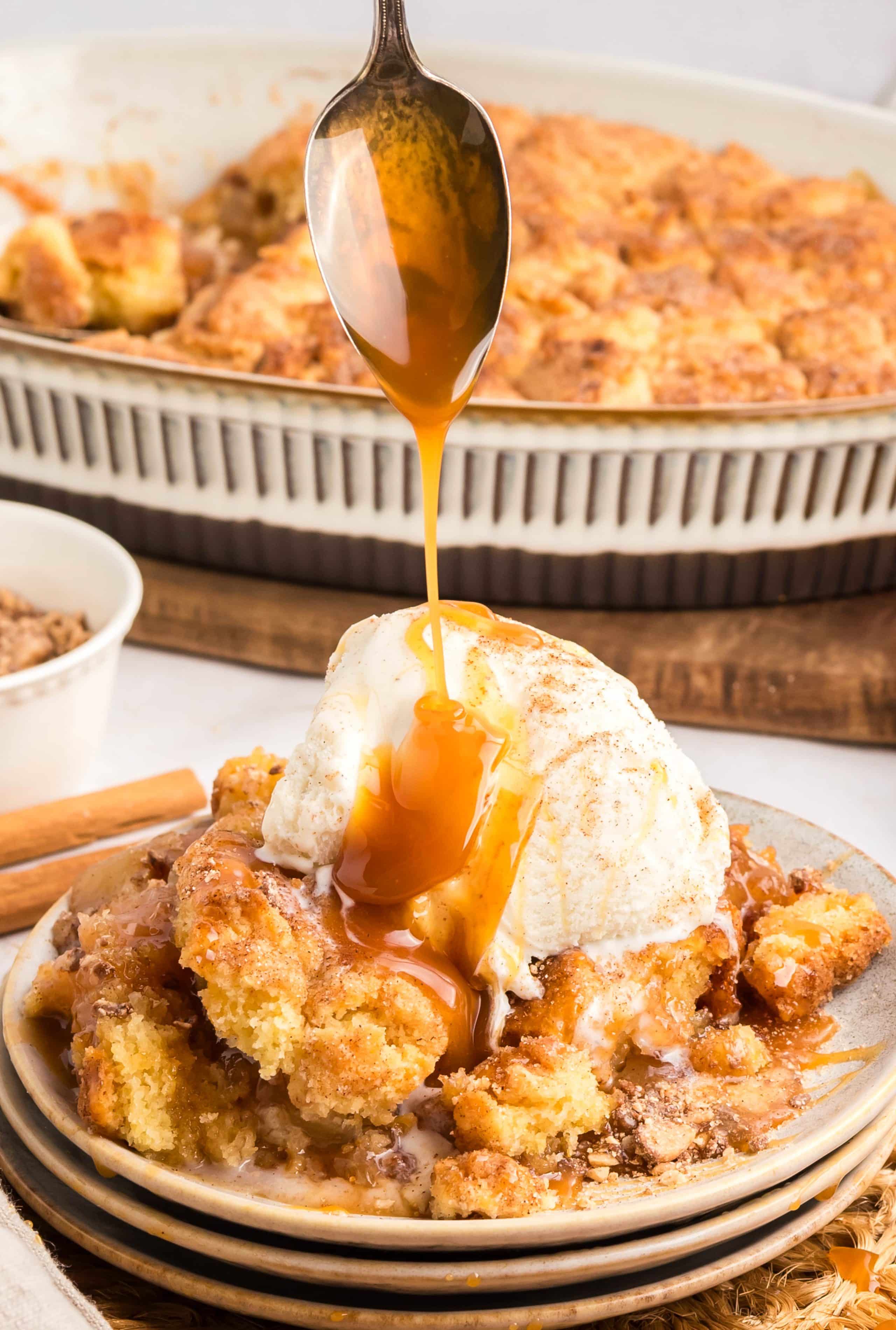 Spoon drizzling caramel over warm snickerdoodle apple cobbler with ice cream.